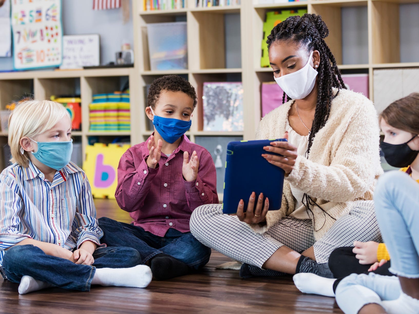 Teacher and students sitting together in a circle on the floor and wearing masks