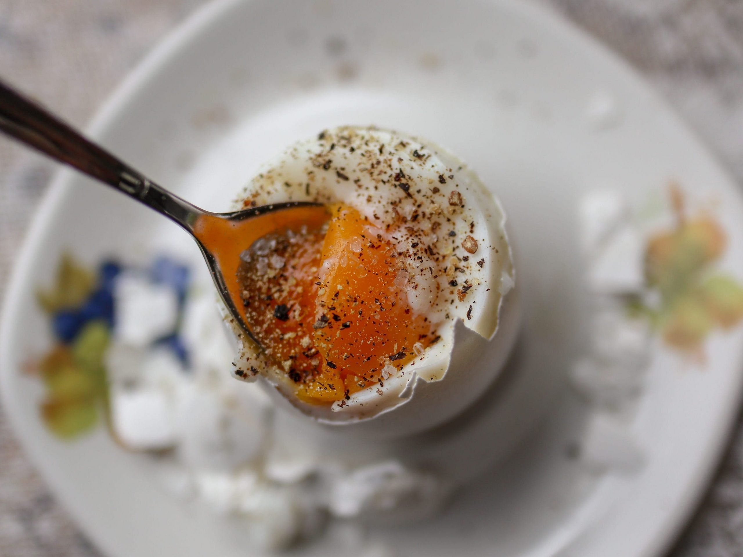 A spoon breaking into a runny, soft boiled egg