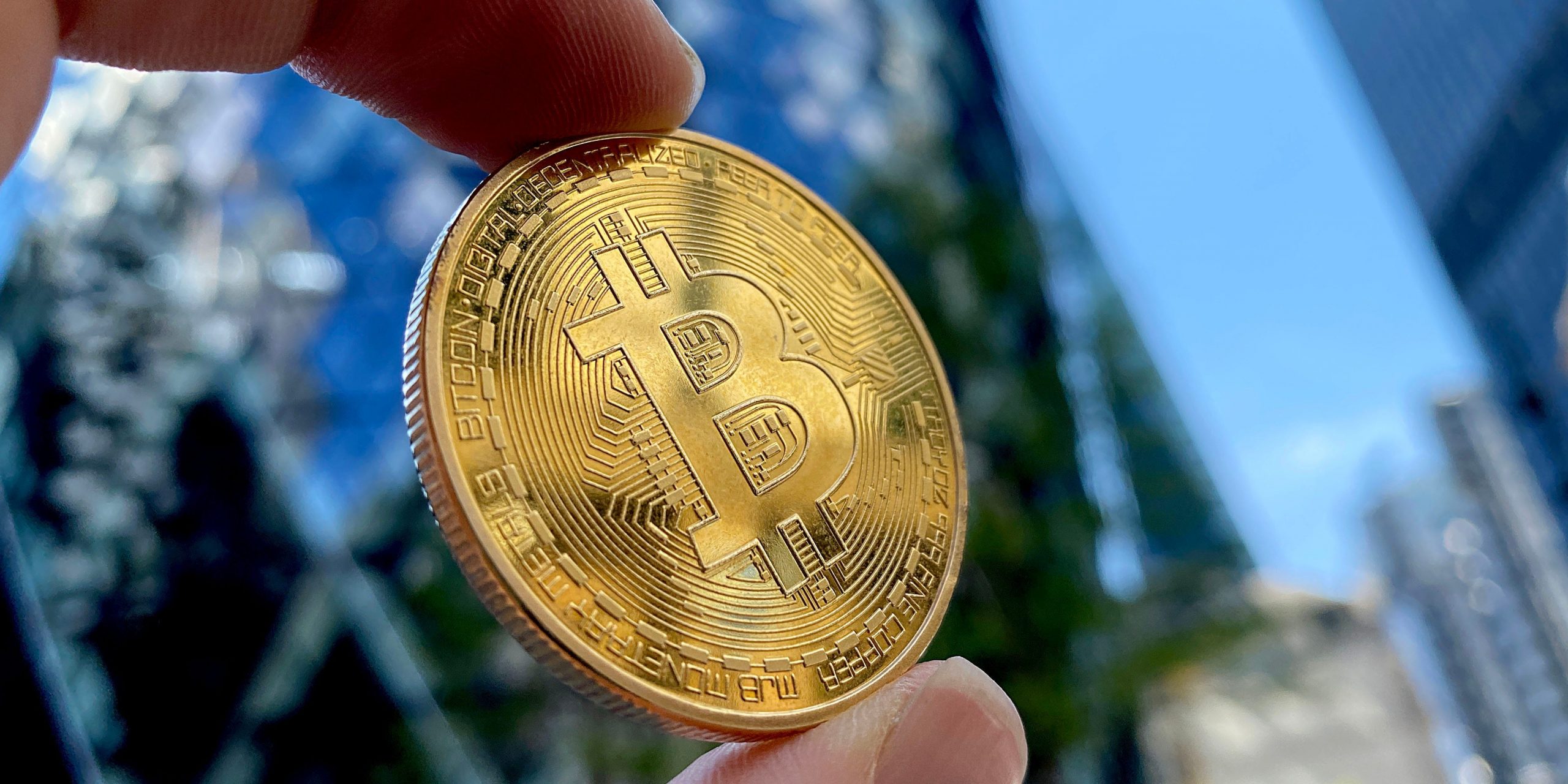 A hand holds a bitcoin toward the sky in this photo representation of the cryptocurrency.