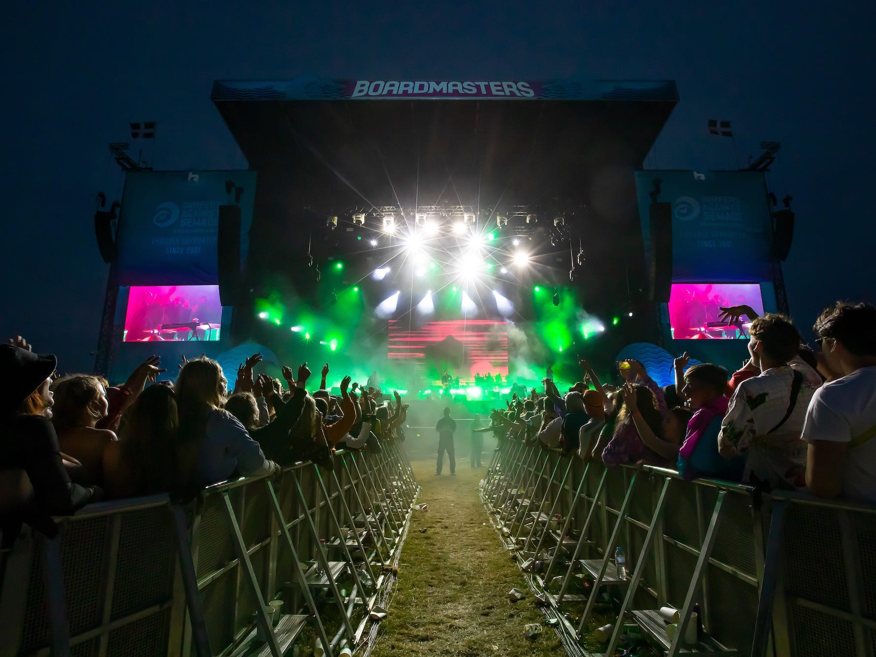 a clearing between packed crowds leads to a stage at Boardmasters where Gorillaz are playing at night/