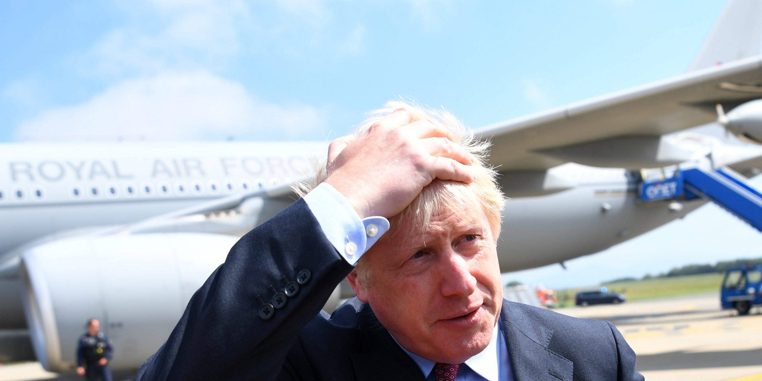 Boris Johnson clutches his hair as he is questioned by Robert Peston on an airstrip. There is an RAF jet behind him.