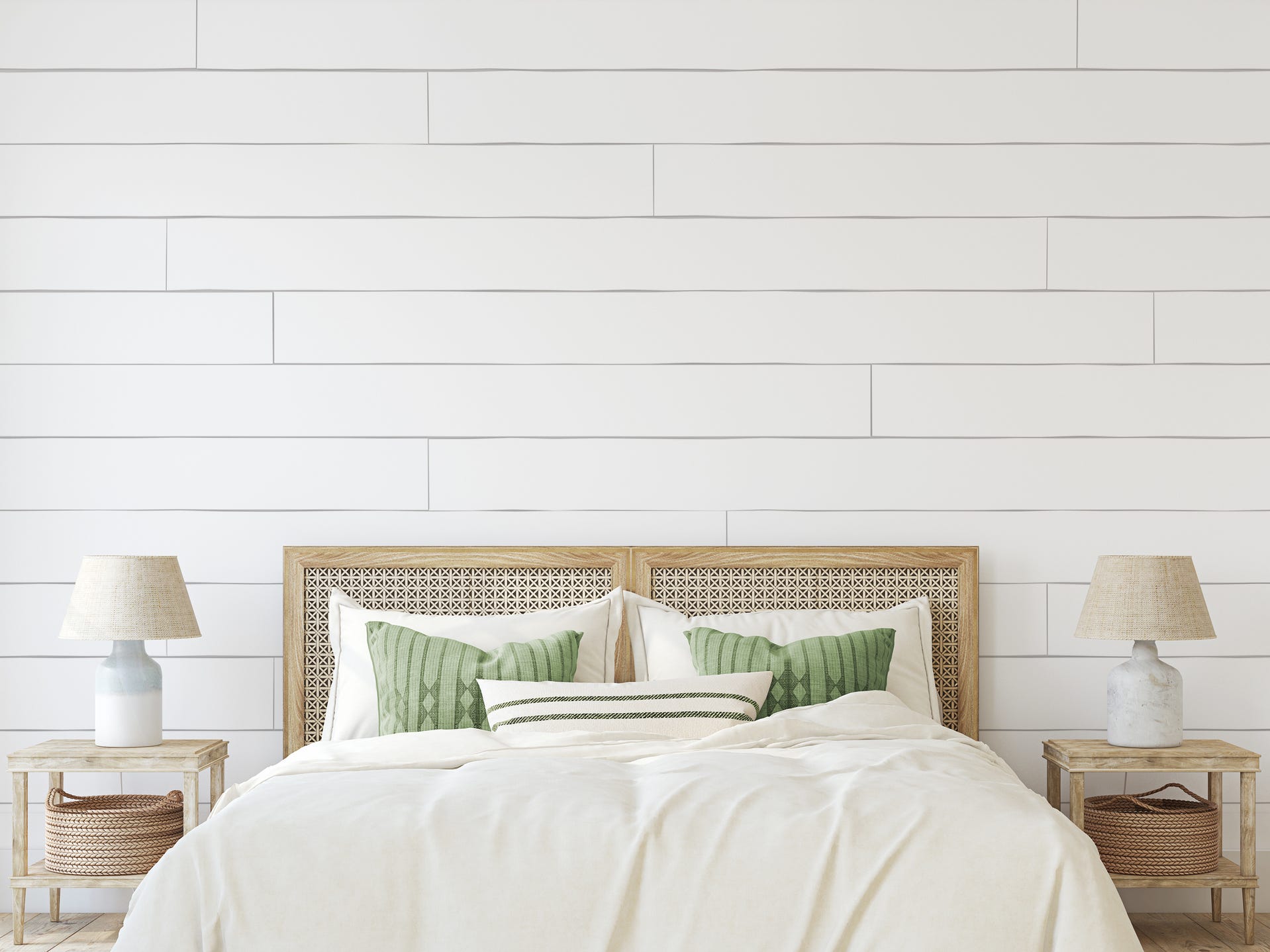 A bed with a cane headboard, green pillows, white bed spread, and matching nightstands with white lamps