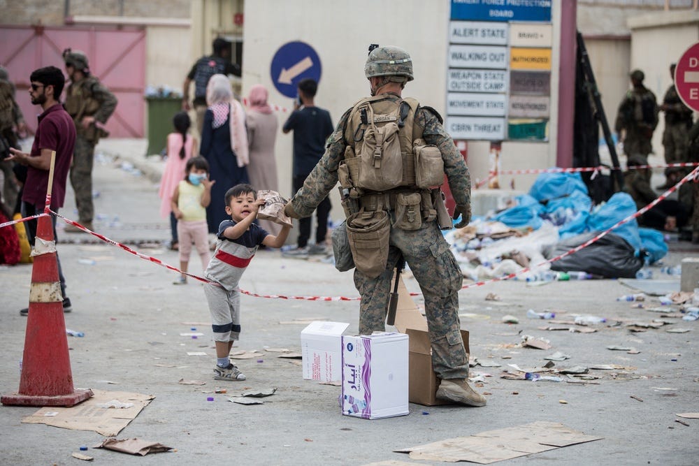 A Marine with the 24th Marine Expeditionary Unit (MEU) provides a meal ready-to-eat to a child during an evacuation at Hamid Karzai International Airport, Kabul, Afghanistan, Aug. 20