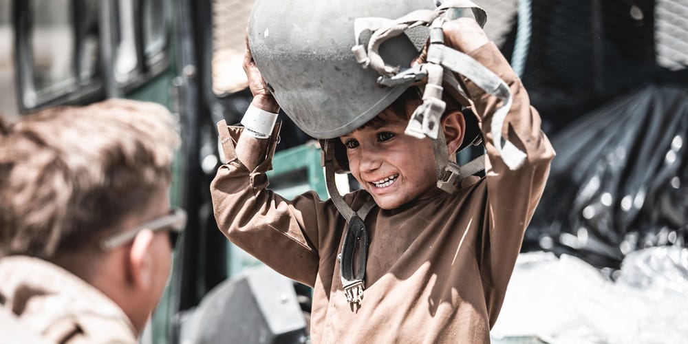 A Marine assigned to Special Purpose Marine Air-Ground Task Force - Crisis Response - Central Command hands a helmet to a child awaiting evacuation at Hamid Karzai International Airport, Afghanistan, Aug. 22, 2021