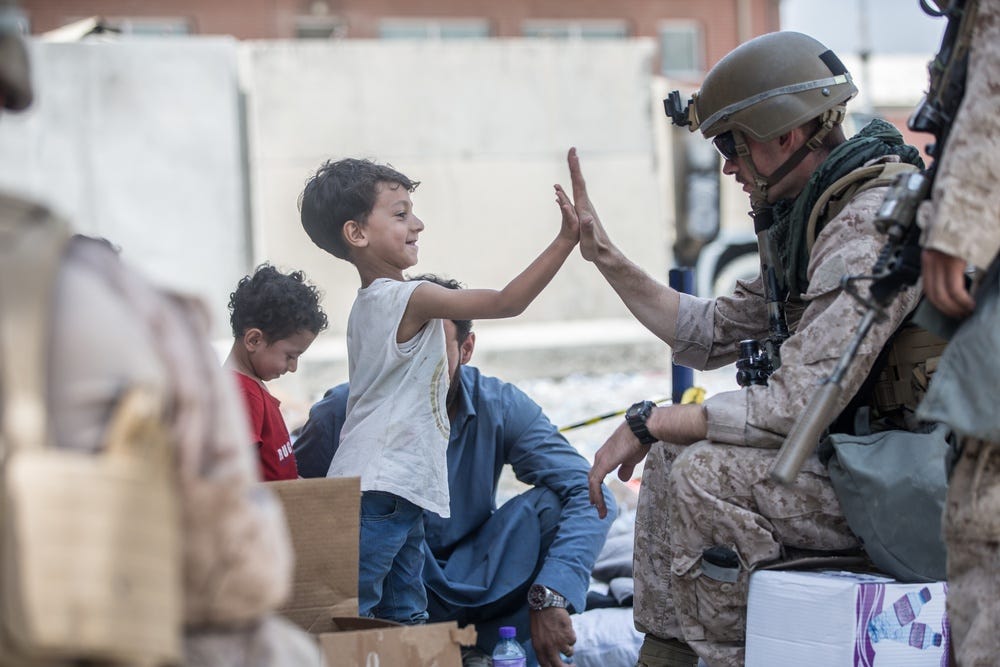 A Marine with Special Purpose Marine Air-Ground Task Force-Crisis Response-Central Command (SPMAGTF-CR-CC) gives a high five to a child during an evacuation at Hamid Karzai International Airport, Kabul, Afghanistan, Aug. 22