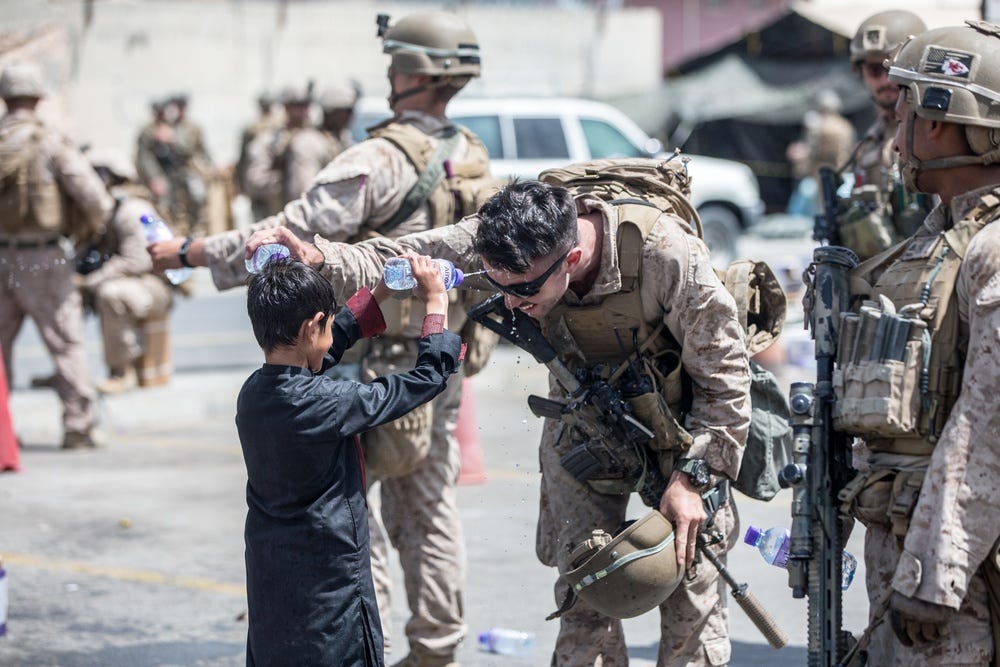 A Marine with Special Purpose Marine Air-Ground Task Force-Crisis Response-Central Command (SPMAGTF-CR-CC) and a child spray water at each other during an evacuation at Hamid Karzai International Airport, Kabul, Afghanistan, Aug. 21