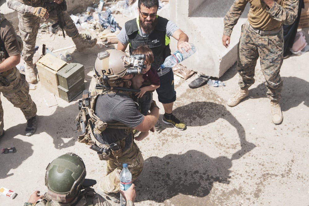 An Airman carries a child at an Evacuation Control Checkpoint during an evacuation at Hamid Karzai International Airport, Kabul, Afghanistan, Aug. 20