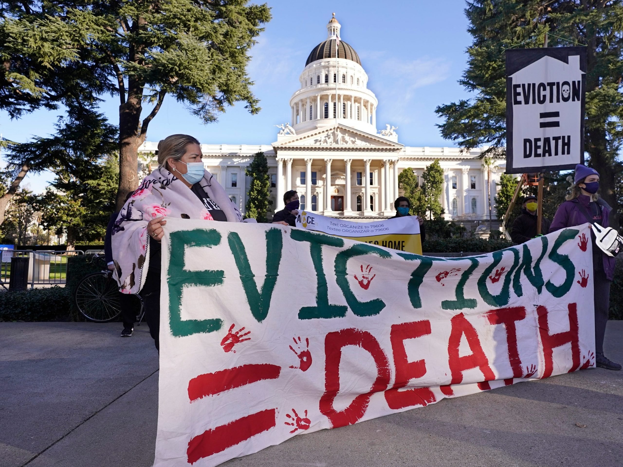 Protesters outside the California Capitol hold a sign that reads "Evictions=Death."