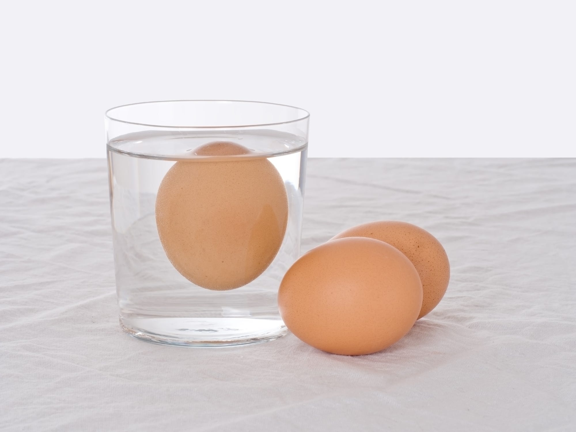 A rotten egg floating in a glass of water, with two other eggs sitting next to it