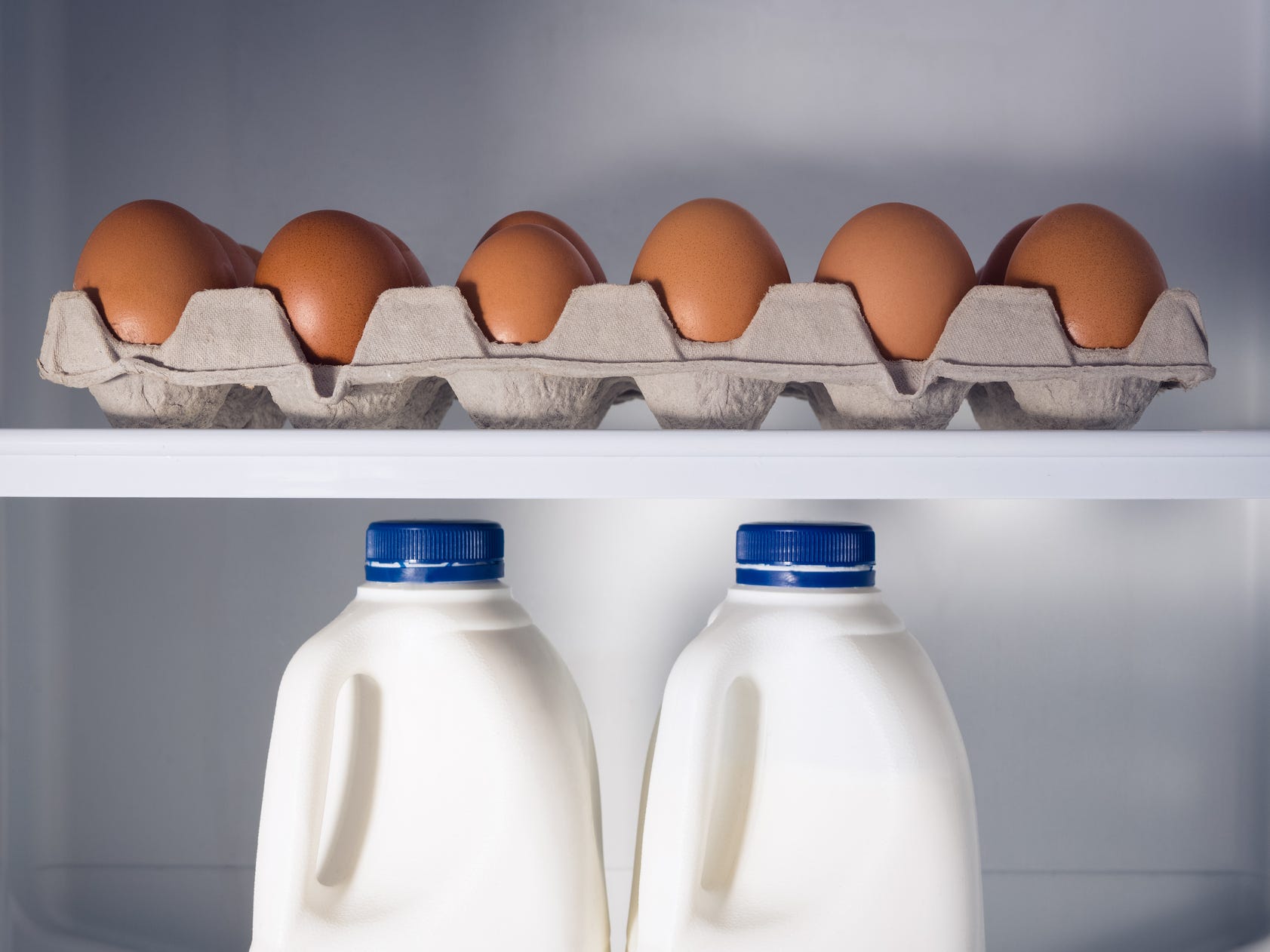 A carton of eggs and two bottles of milk inside of a refrigerator