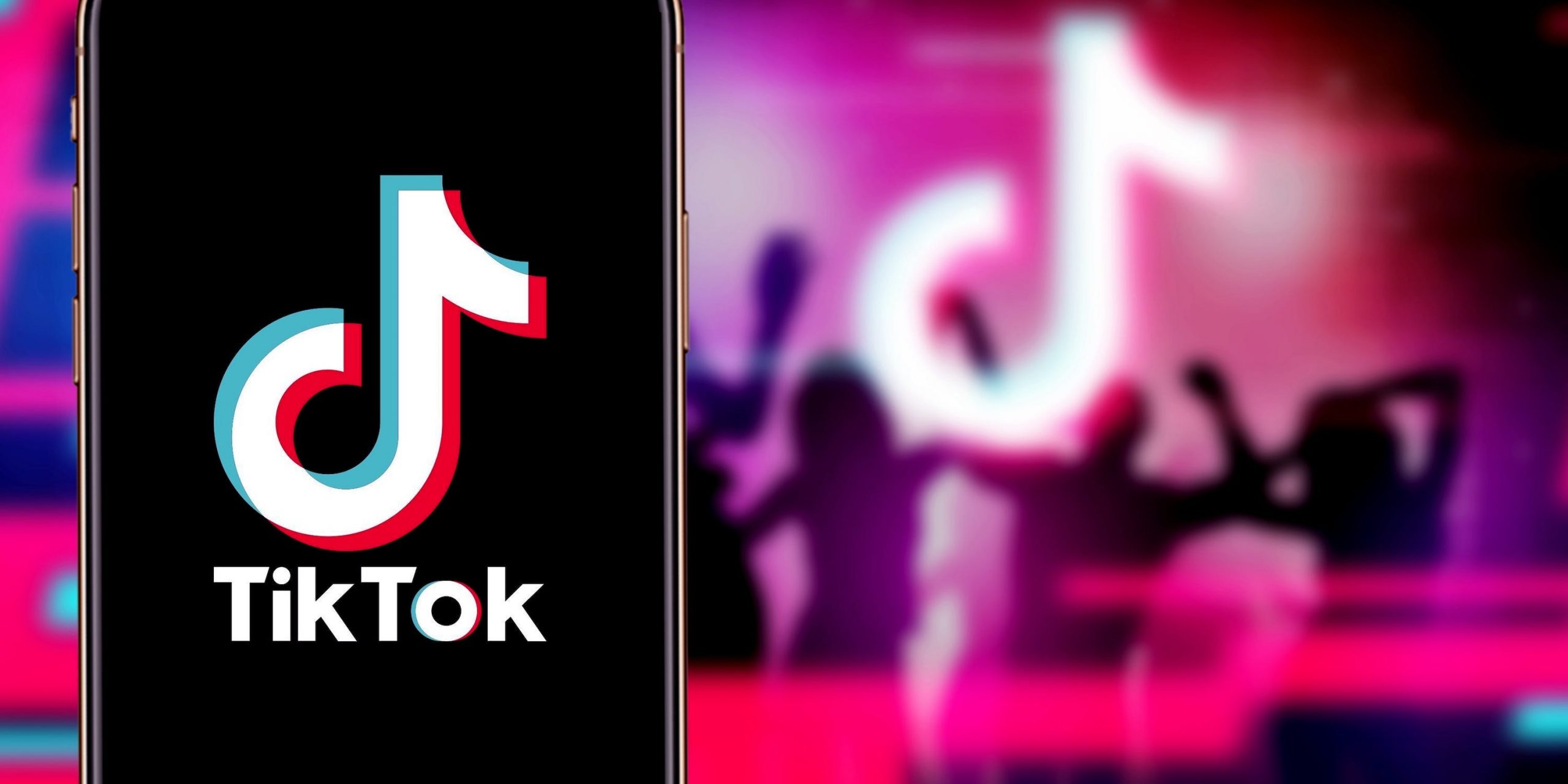 An iPhone displaying the TikTok logo. In the background, silhouettes dance around a TikTok logo.