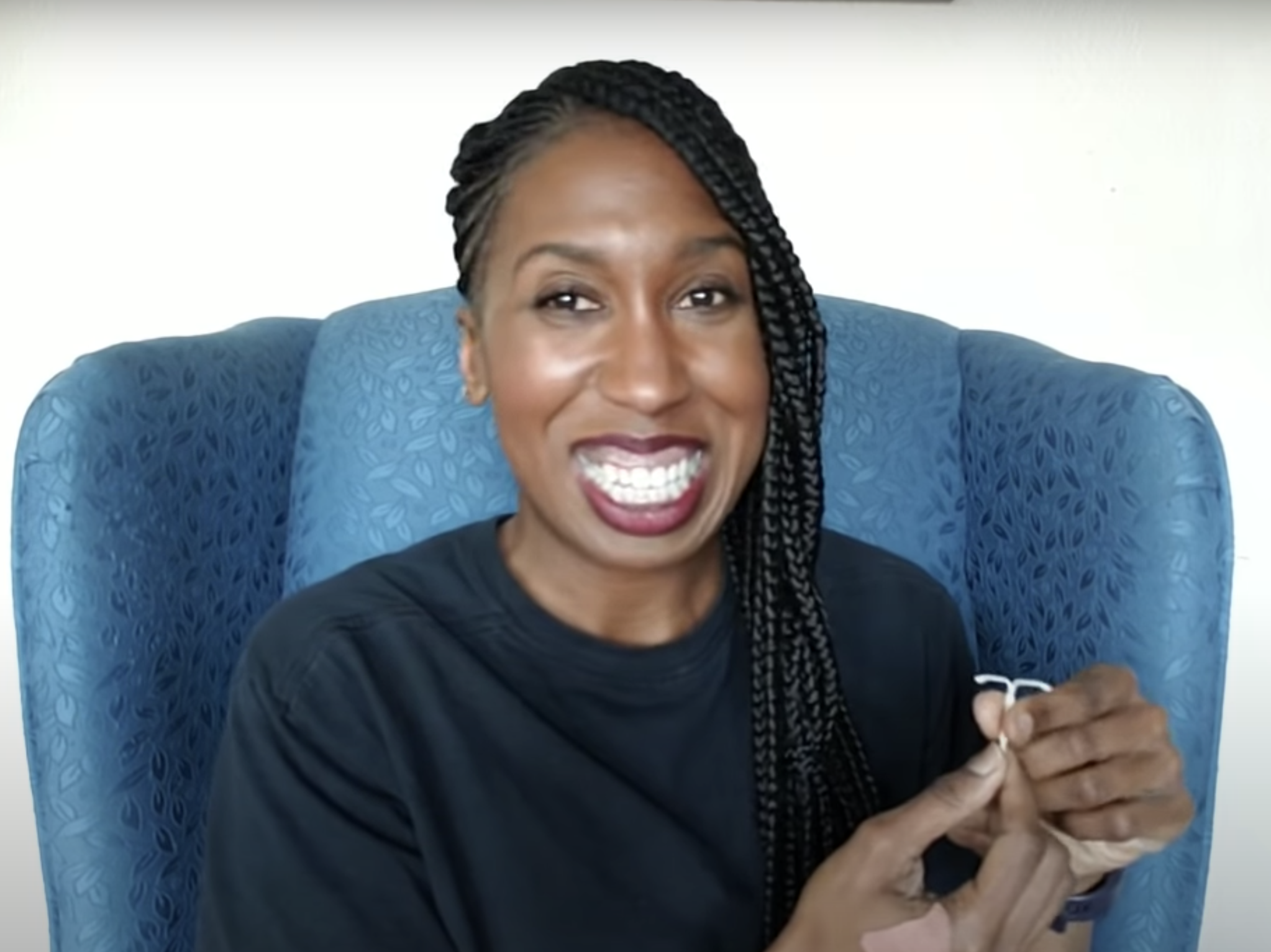 A woman smiling and sitting in a blue armchair holding an IUD to her left.