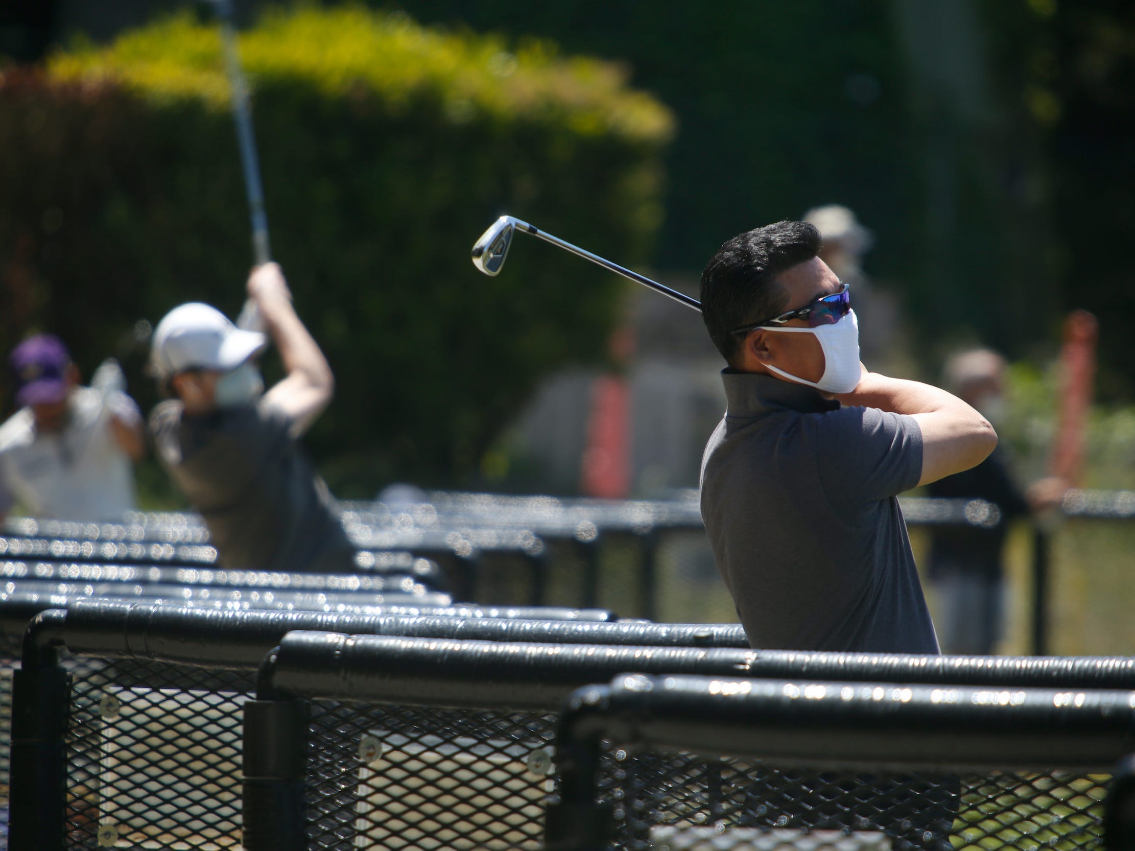 Man wearing a face mask swings golf club at driving range