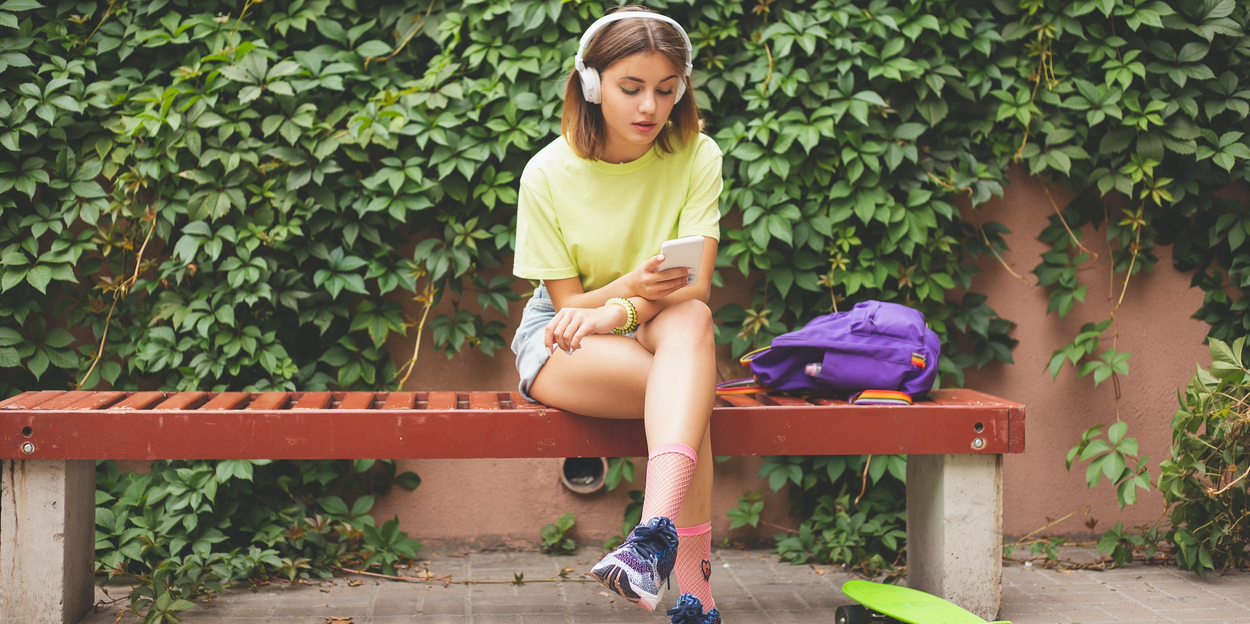 Teen skateboarder using phone with headphones outside