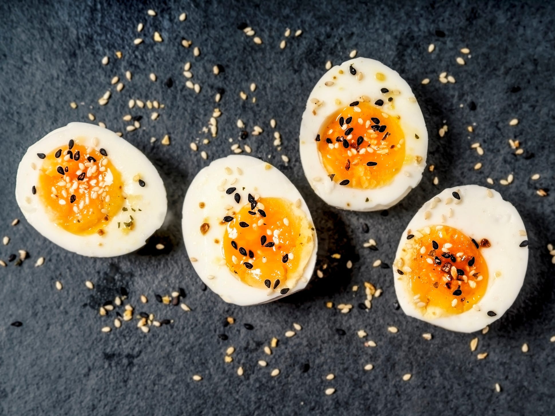 Halved hard-boiled eggs topped with black and white sesame seeds on a slate background