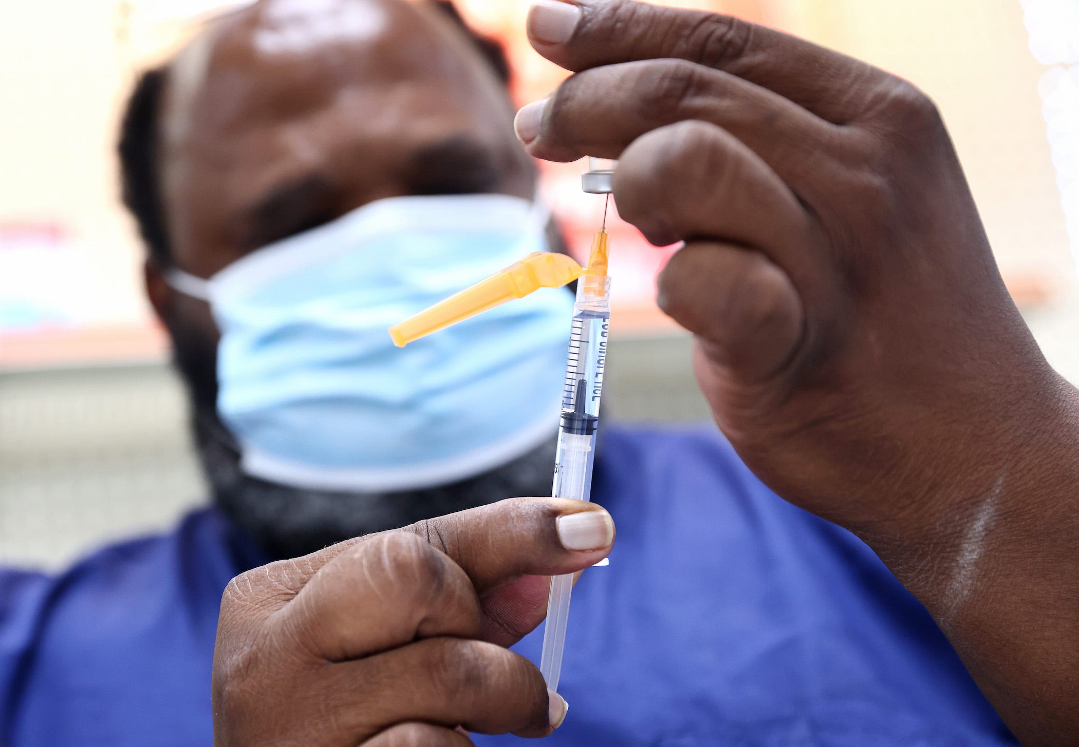 A COVID-19 vaccination dose is being loaded into a syringe by a healthcare worker in scrubs and a mask