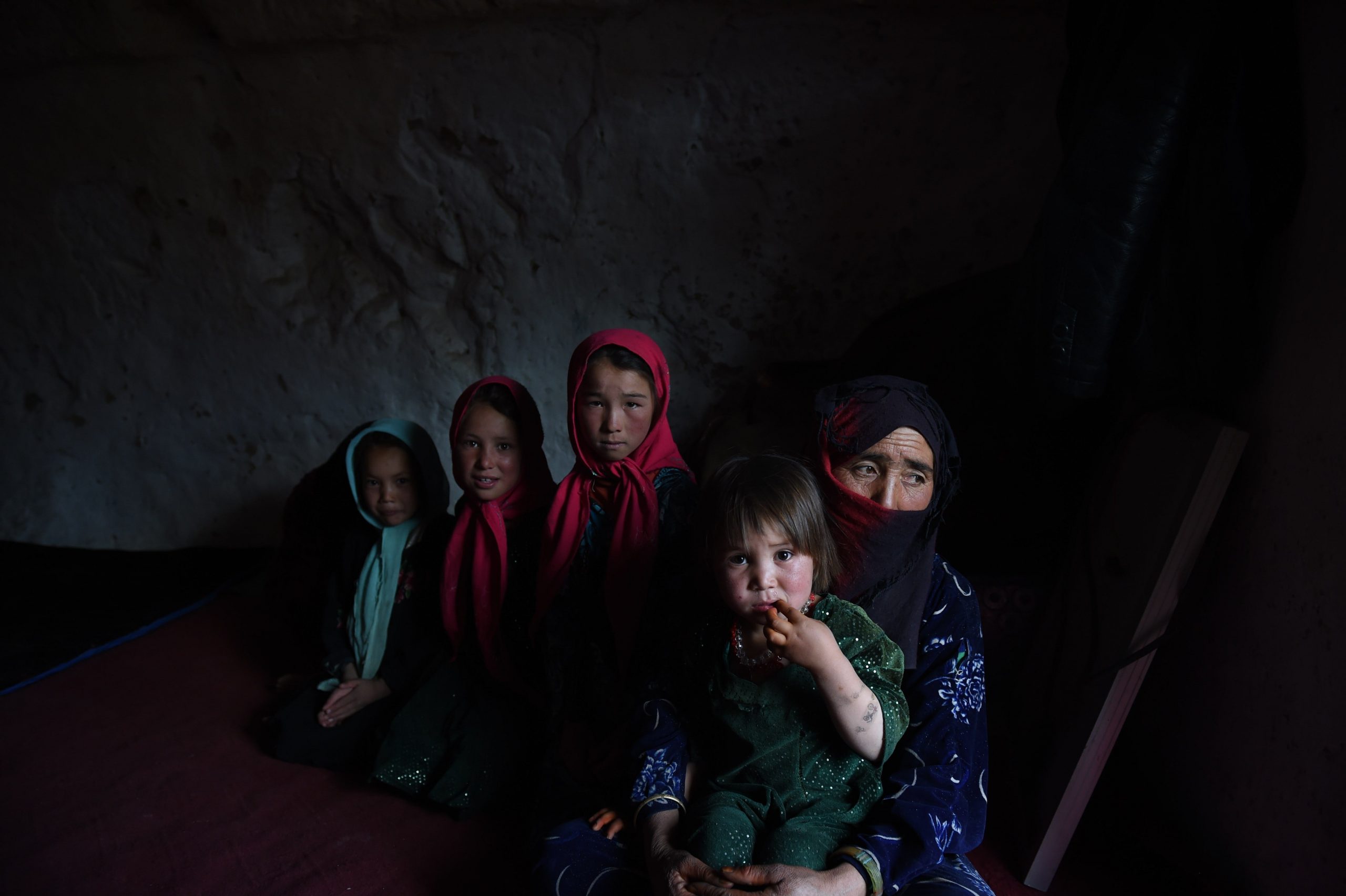 A  Hazara Afghan woman sits with her children inside their cave in the old city of Bamiyan, on June 19, 2015.