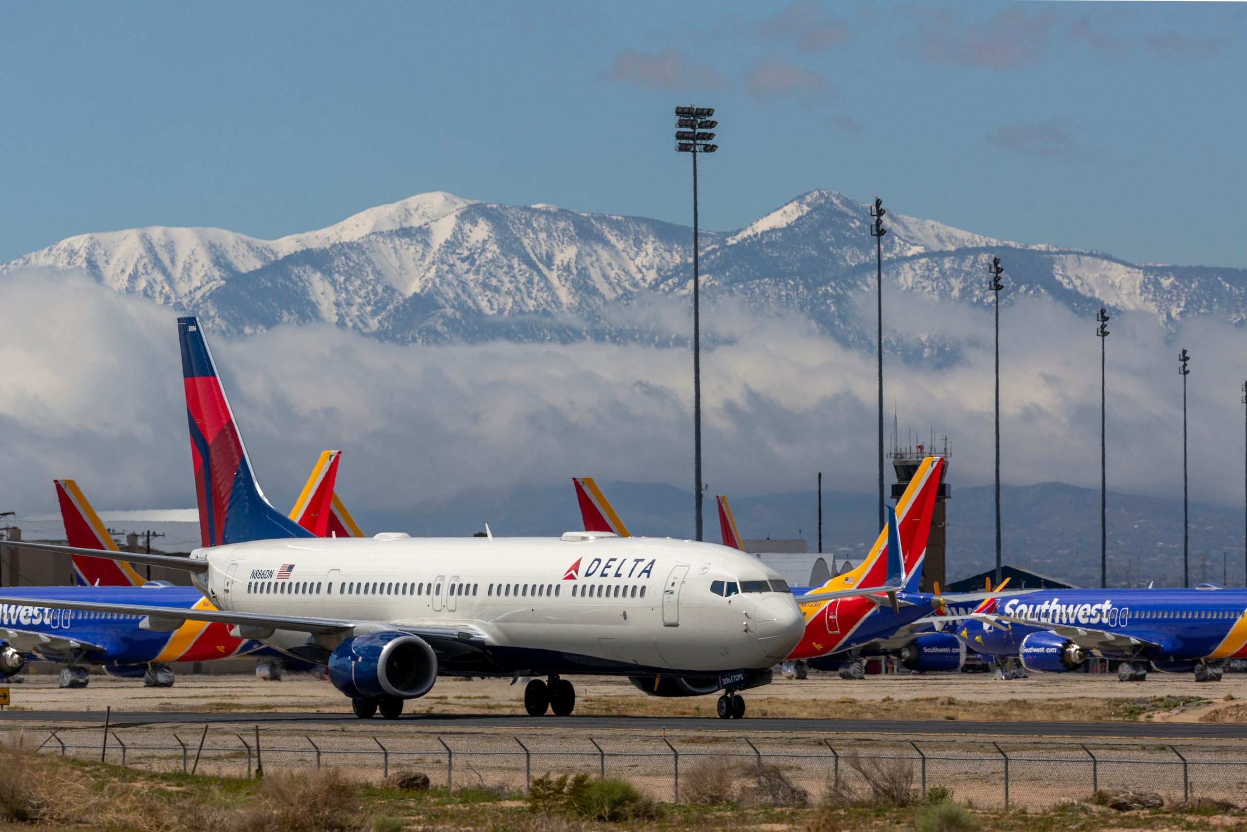 A Delta Air Lines jet taxis along the runway with snowy mountains in the background