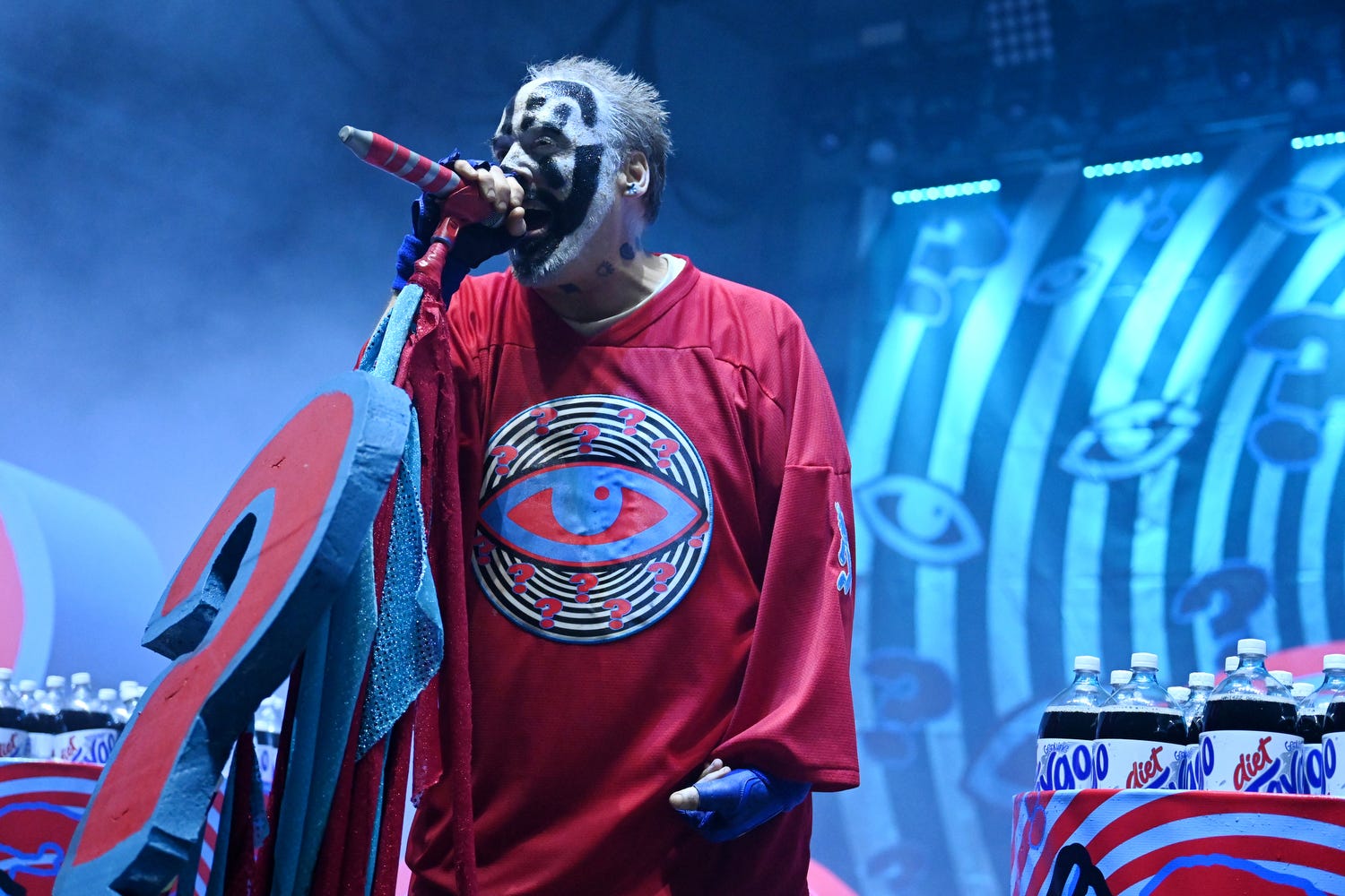 Insane Clown Possee member Violent J, in a red t-shirt, sings into a microphone onstage, with fog surrounding.