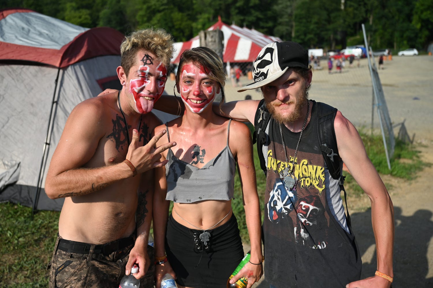 Three juggalos with face paint pose in front of tents.