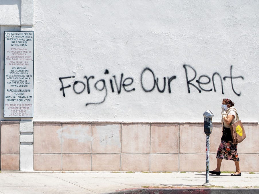 A woman walks past a wall in Los Angeles that has graffiti reading "Forgive Our Rent"
