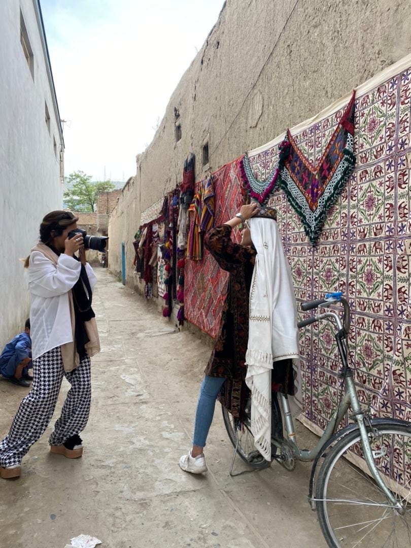 A woman is seen photographing a subject in an narrow street.