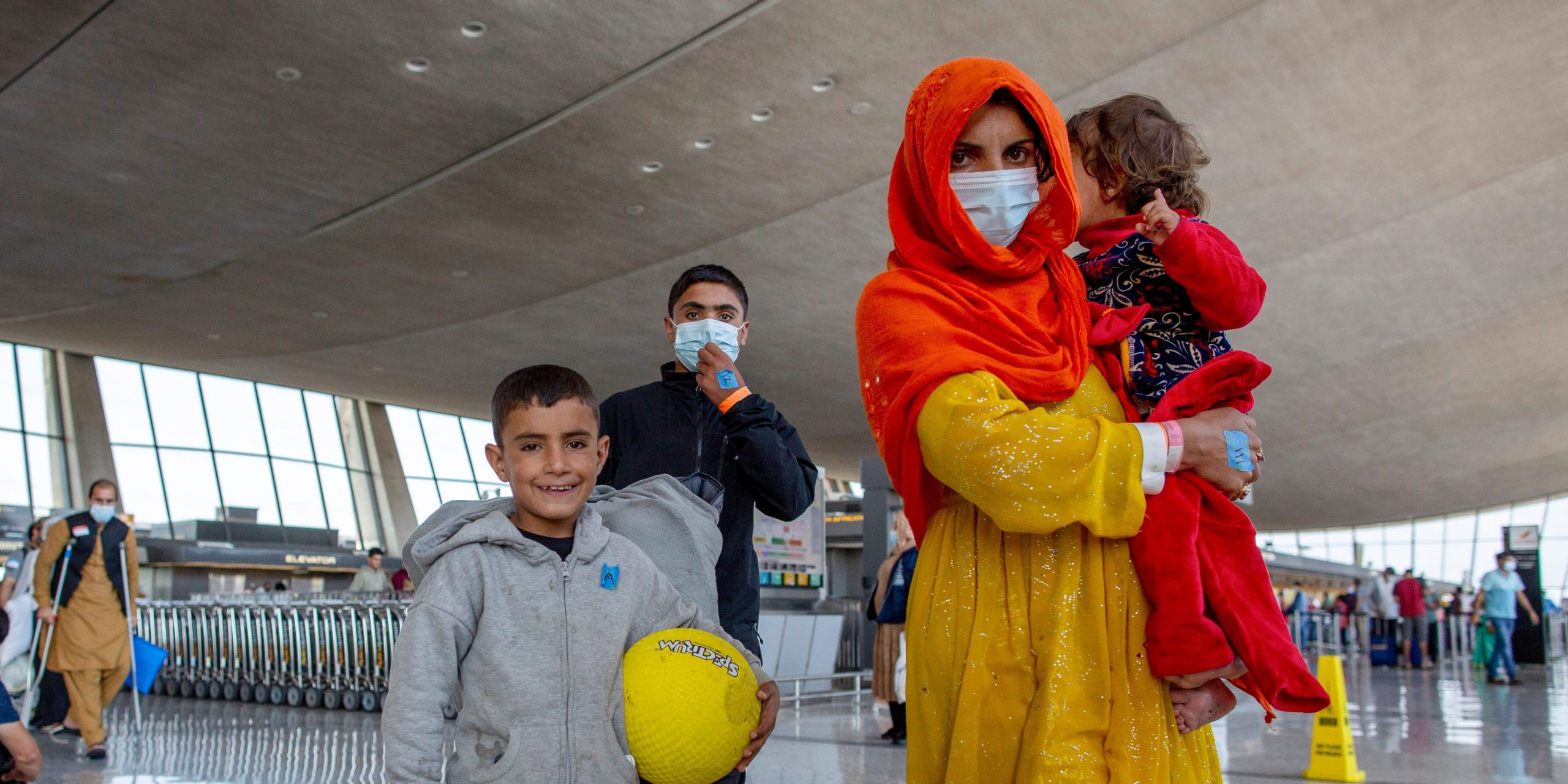 An Afghan woman carries a child and another child walks beside her through the Dulles airport.