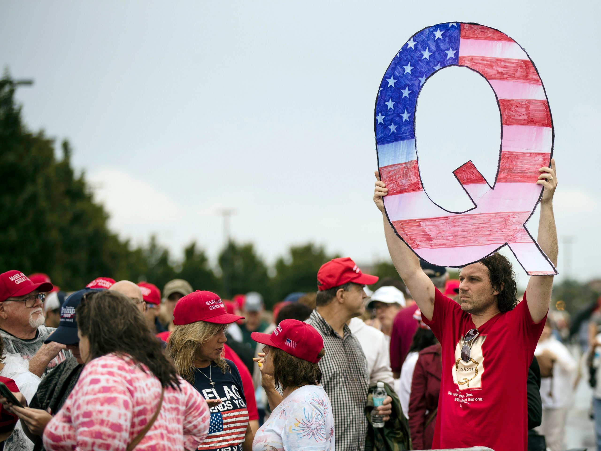 In this Aug. 2, 2018, file photo, a protester holds a Q sign waits in line with others to enter a campaign rally with President Donald Trump in Wilkes-Barre, Pa.