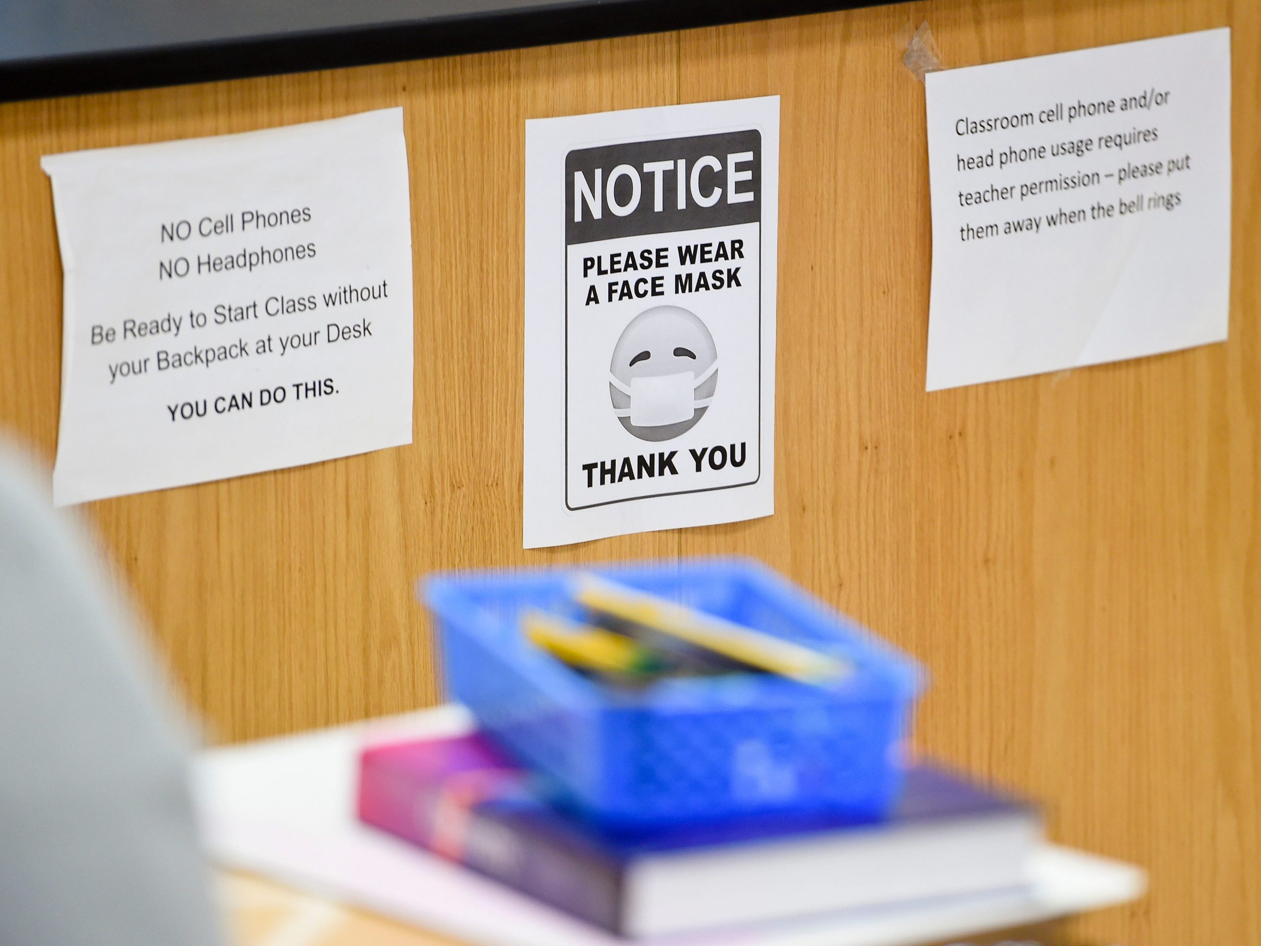 A sign reads 'Please wear a face mask' in a classroom.