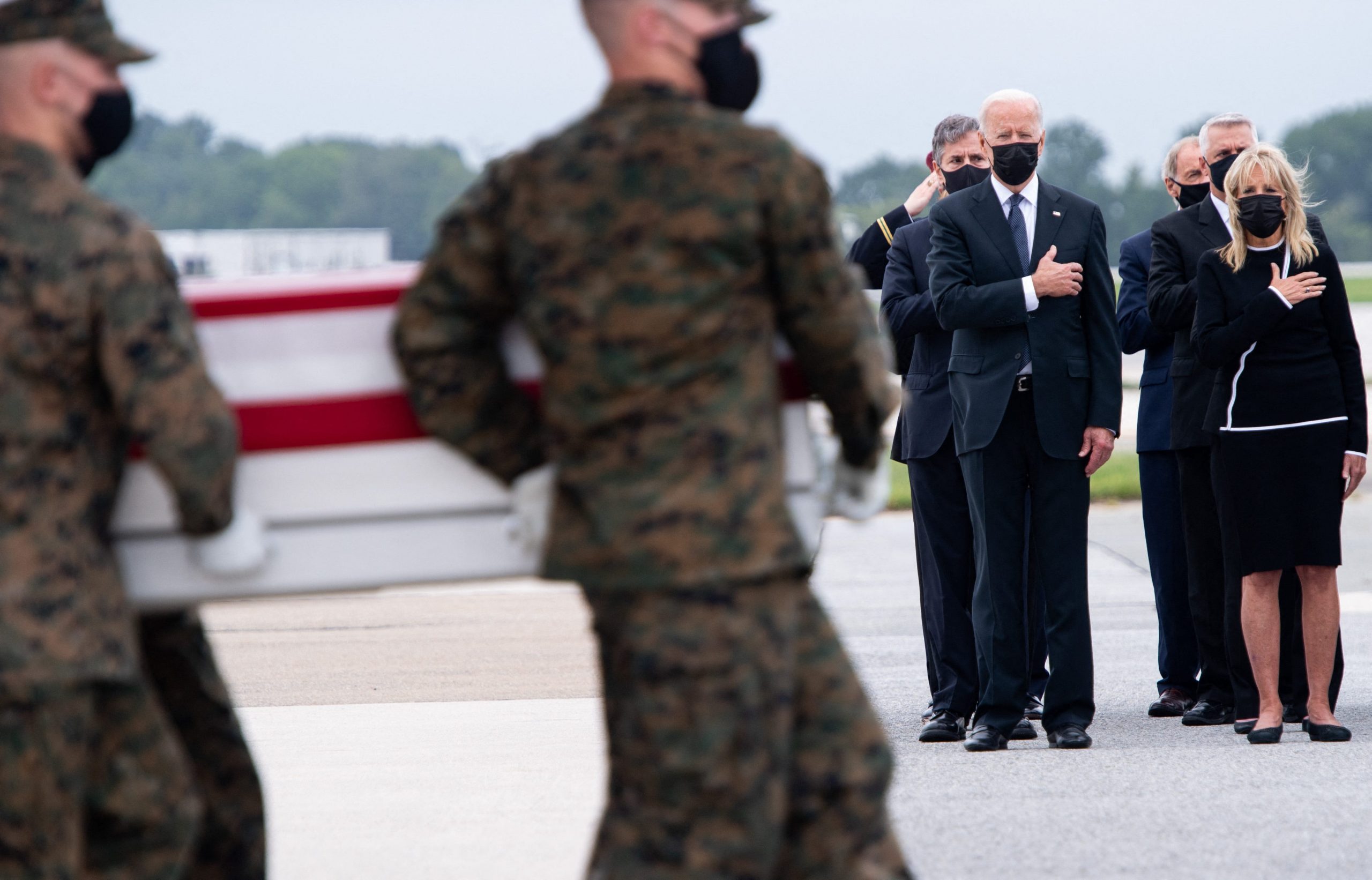 us service members carry a us flag-laden casket as joe Biden jill biden and others look on