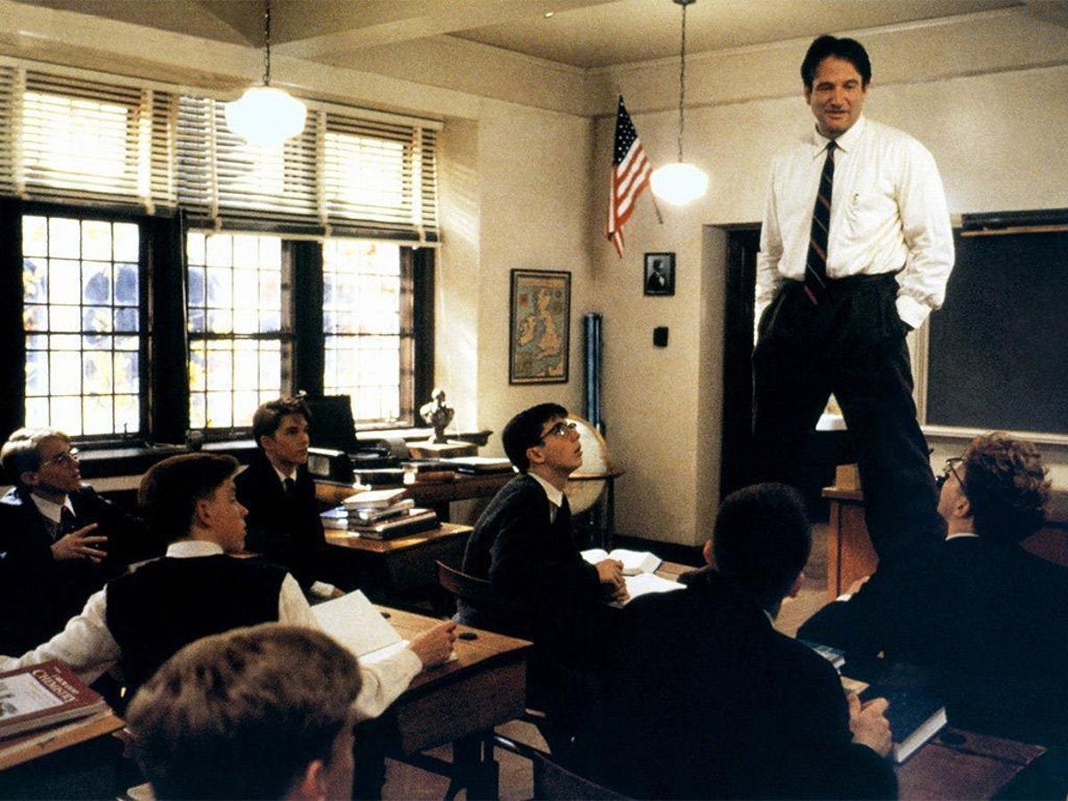 Robin Williams in a shirt and tie standing on a desk