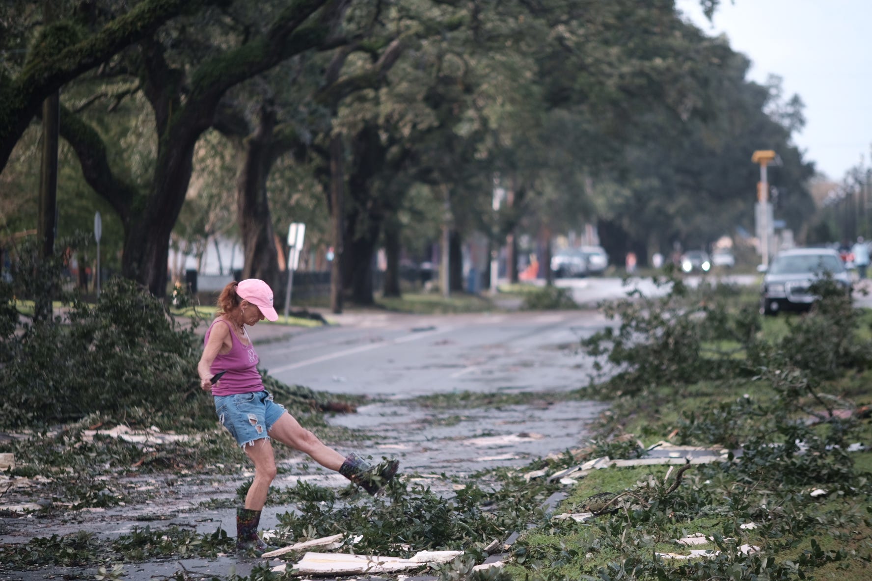 A woman is seen kicking fallen branches from the side of the road.