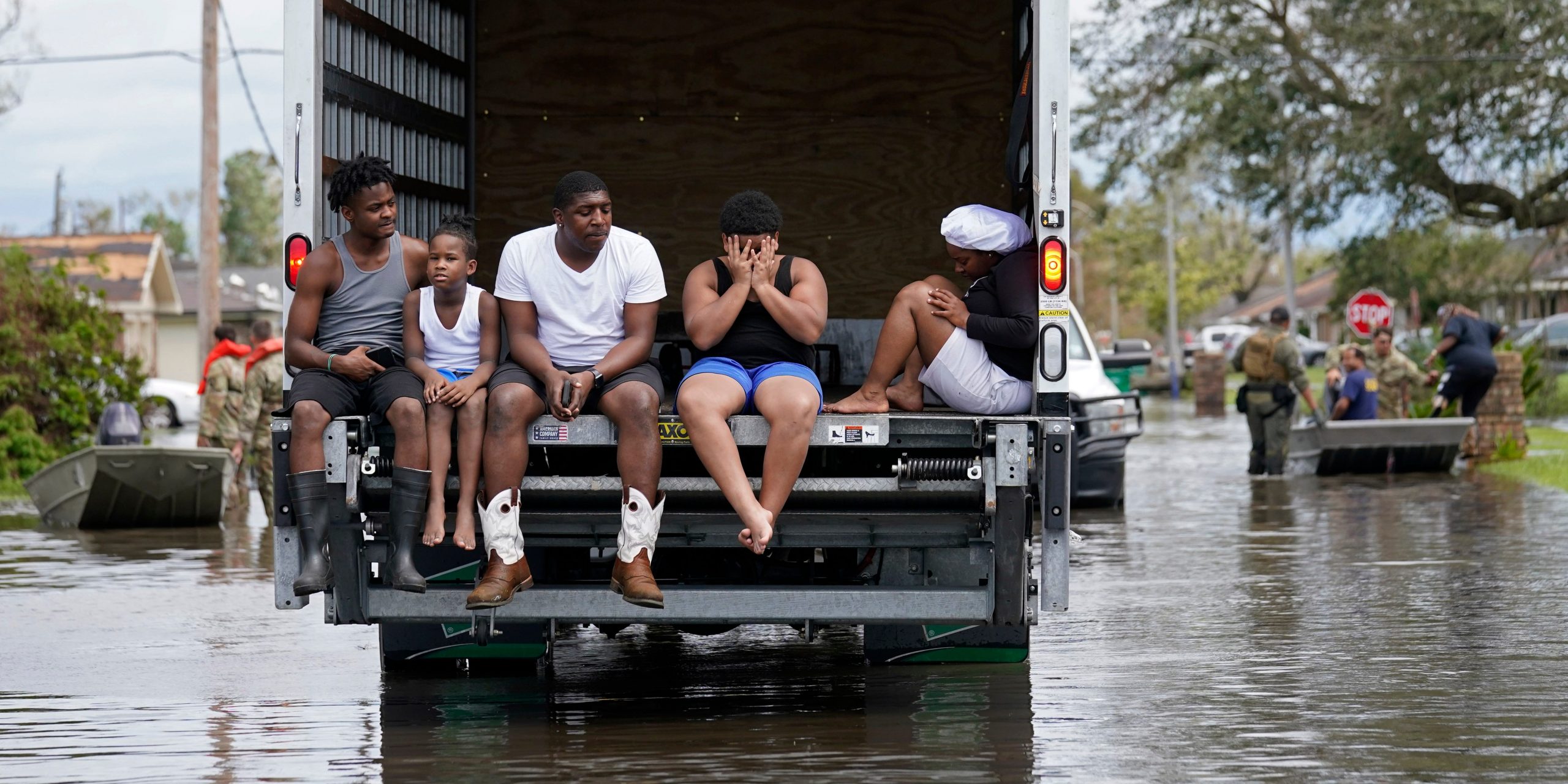 A group of people sit in the back of a truck amid flood waters.