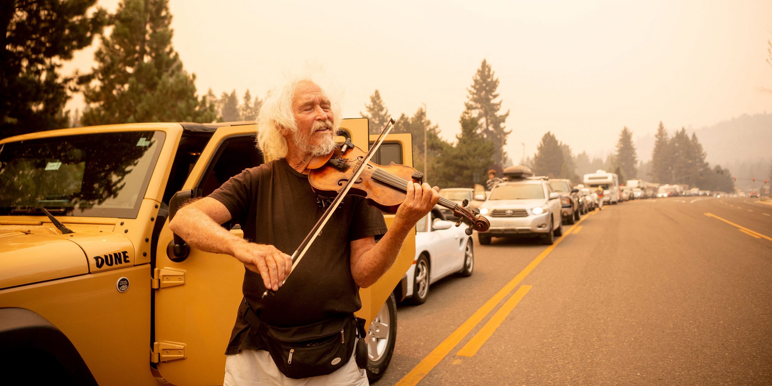 Mel Smothers plays the violin while stuck in traffic with evacuees as residents attempt to flee the Caldor fire in South Lake Tahoe, California on on August 30, 2021. - At least 650 structures have burned and thousands more are threatened as the Caldor fire moves into the resort community of South Lake Tahoe, California.