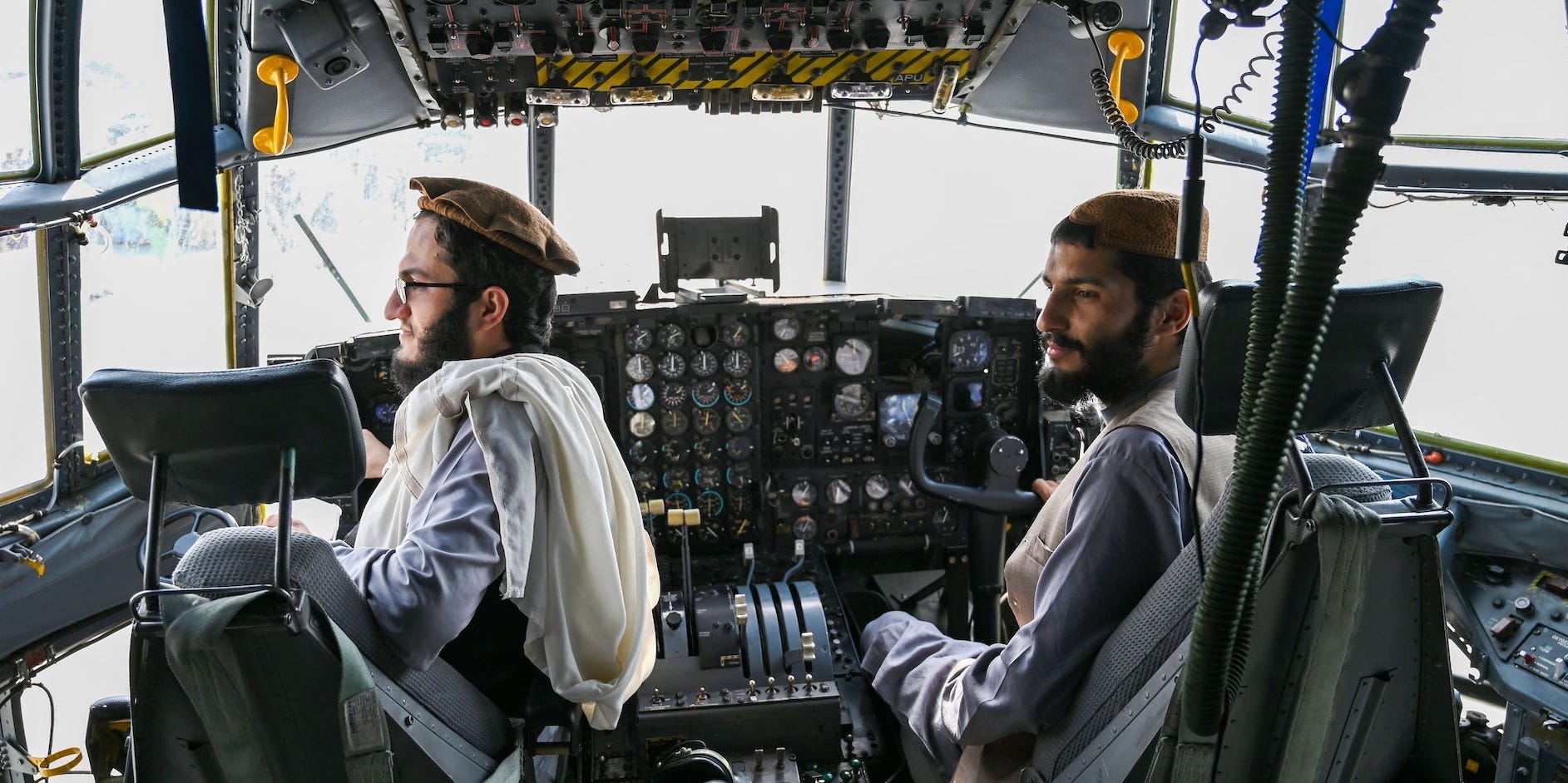 Two Taliban fighters sit in the chairs in a jet cockpit