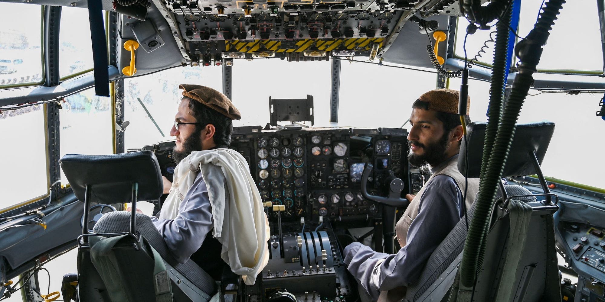 Two Taliban fighters sit in the chairs in a jet cockpit