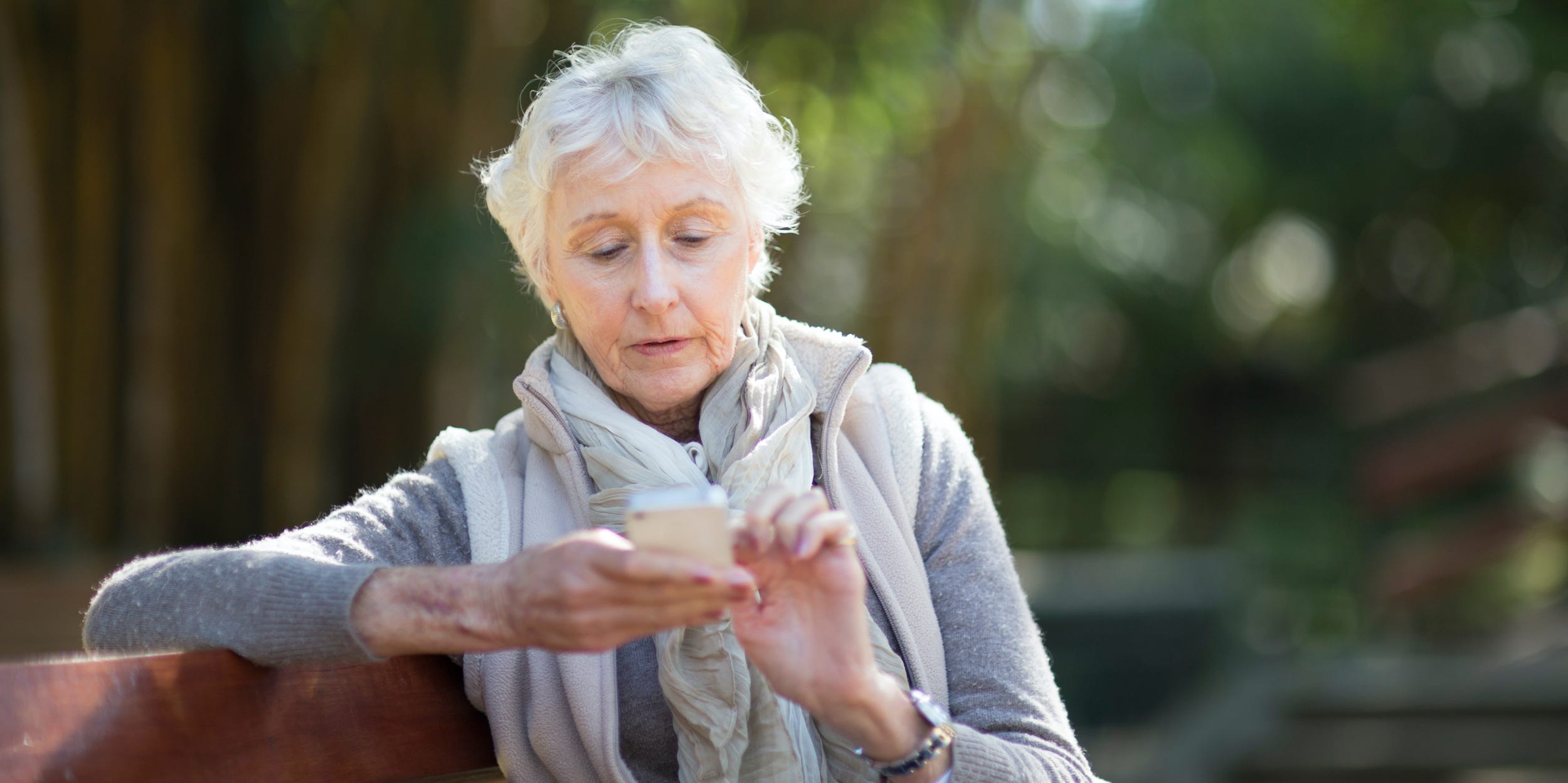 Senior woman texting on smartphone on park bench