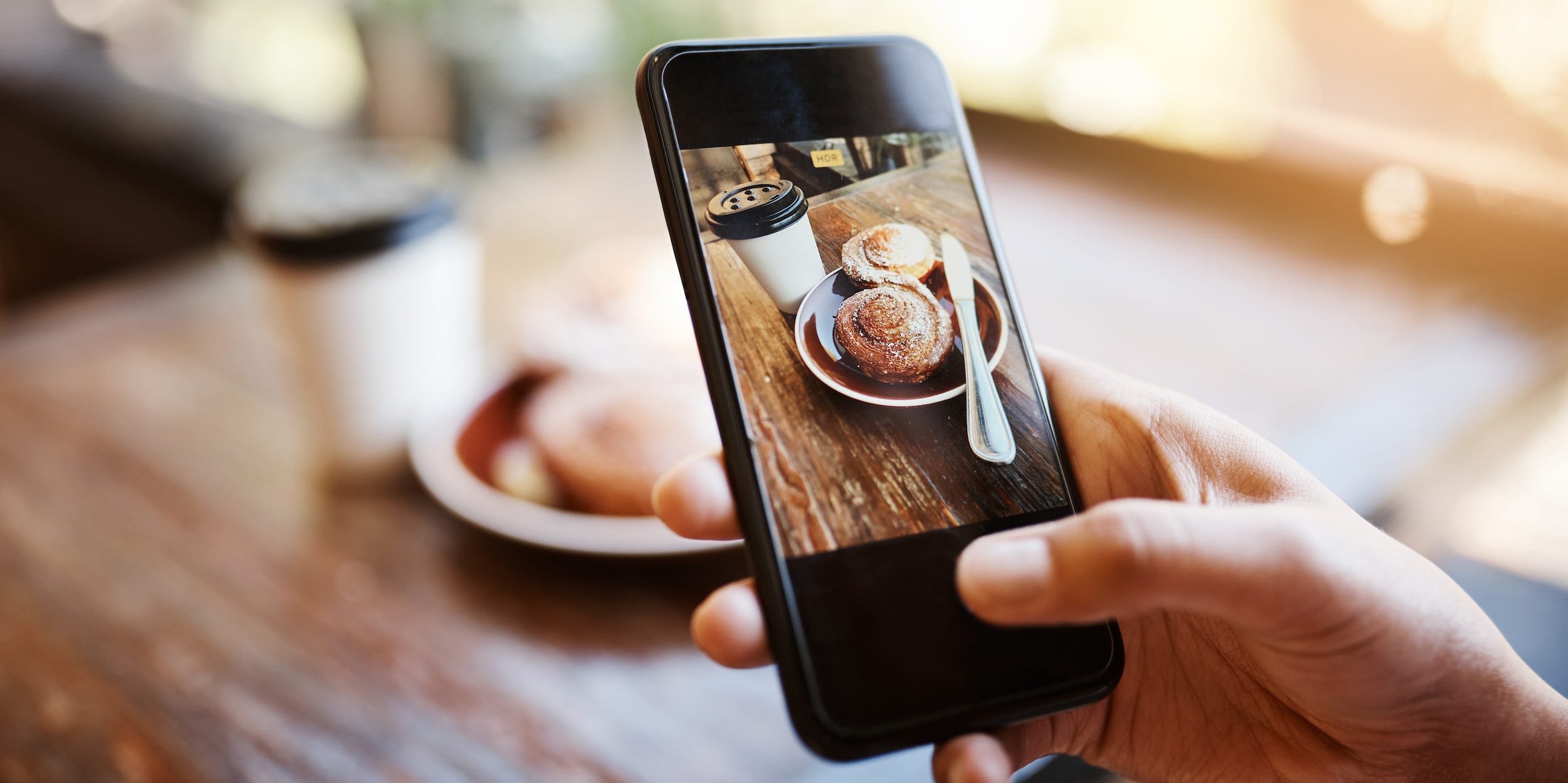 hands taking photo of muffin and coffee on smartphone at cafe