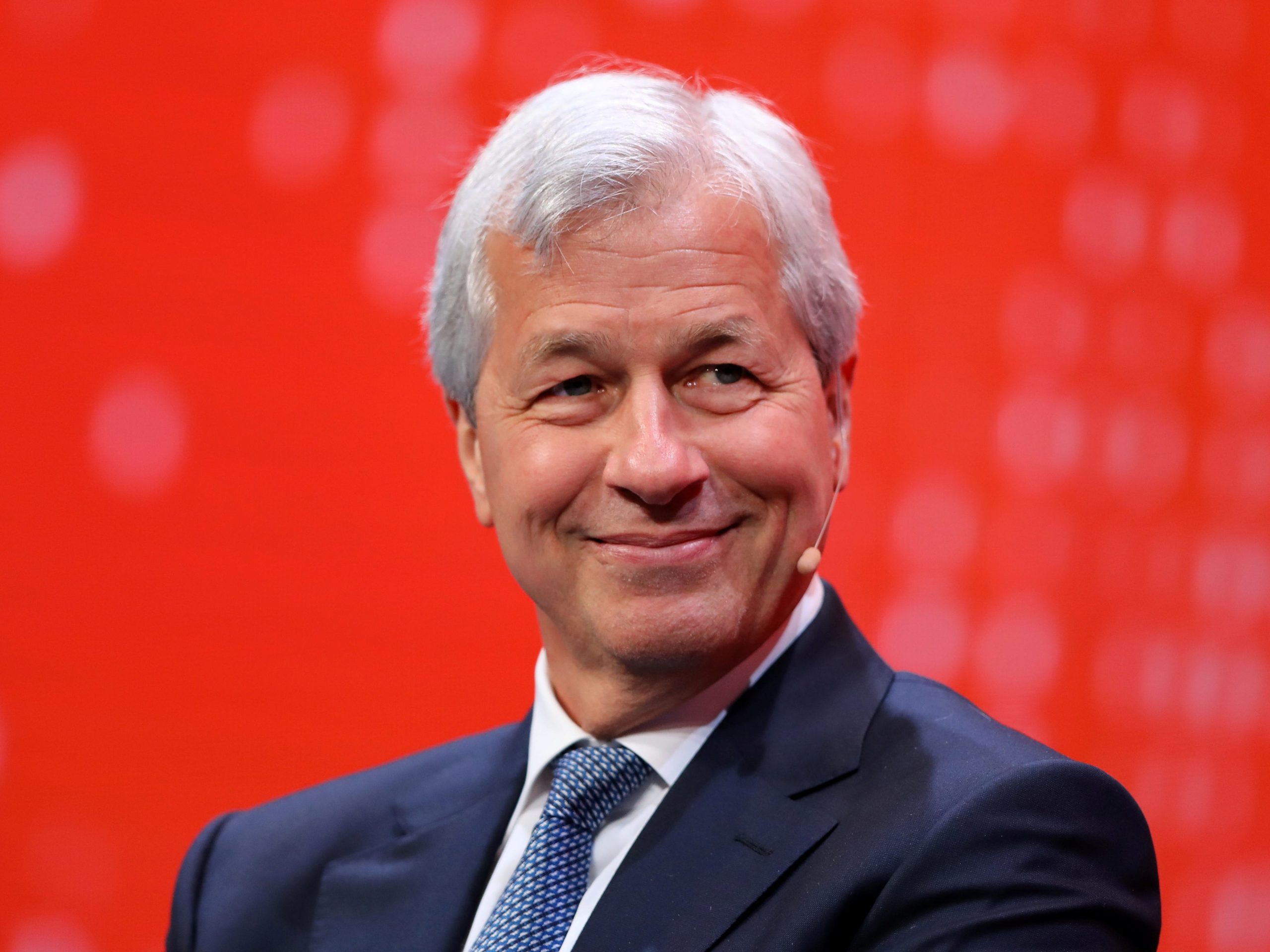 Jamie Dimon smiling and looking to the right against a red background