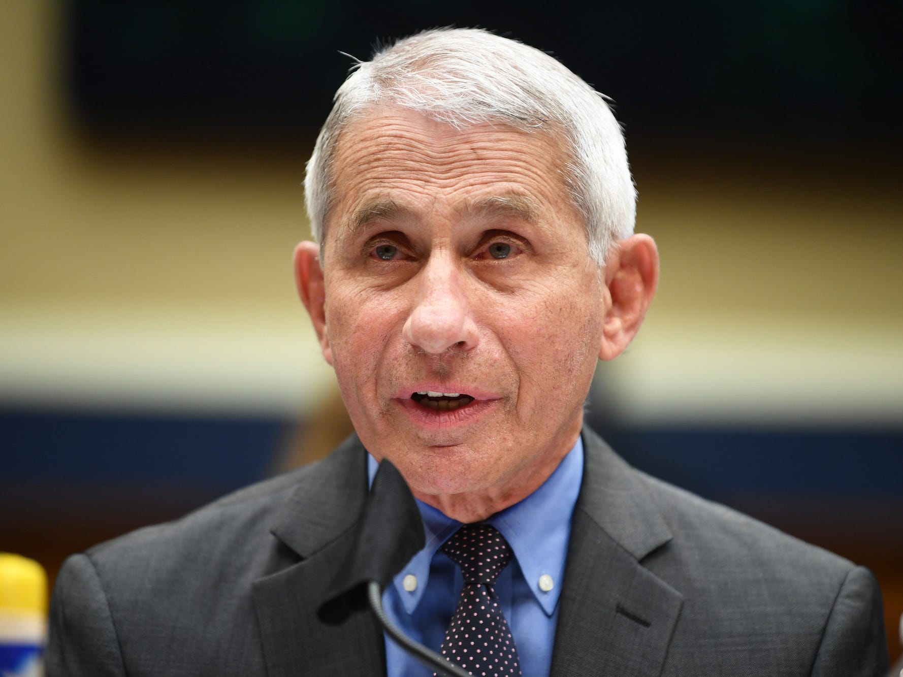 A file image of Dr. Anthony Fauci shows him wearing a blue shirt and black tie and grey suit jacket, speaking into a microphone.