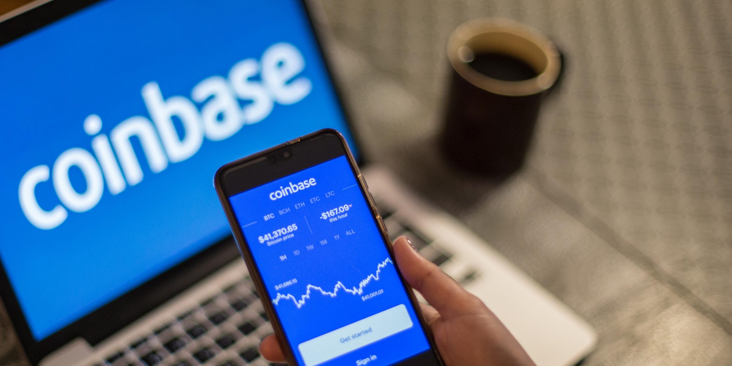 In this photo illustration a Coinbase App and logo is seen displayed on a smartphone and a laptop in the background.