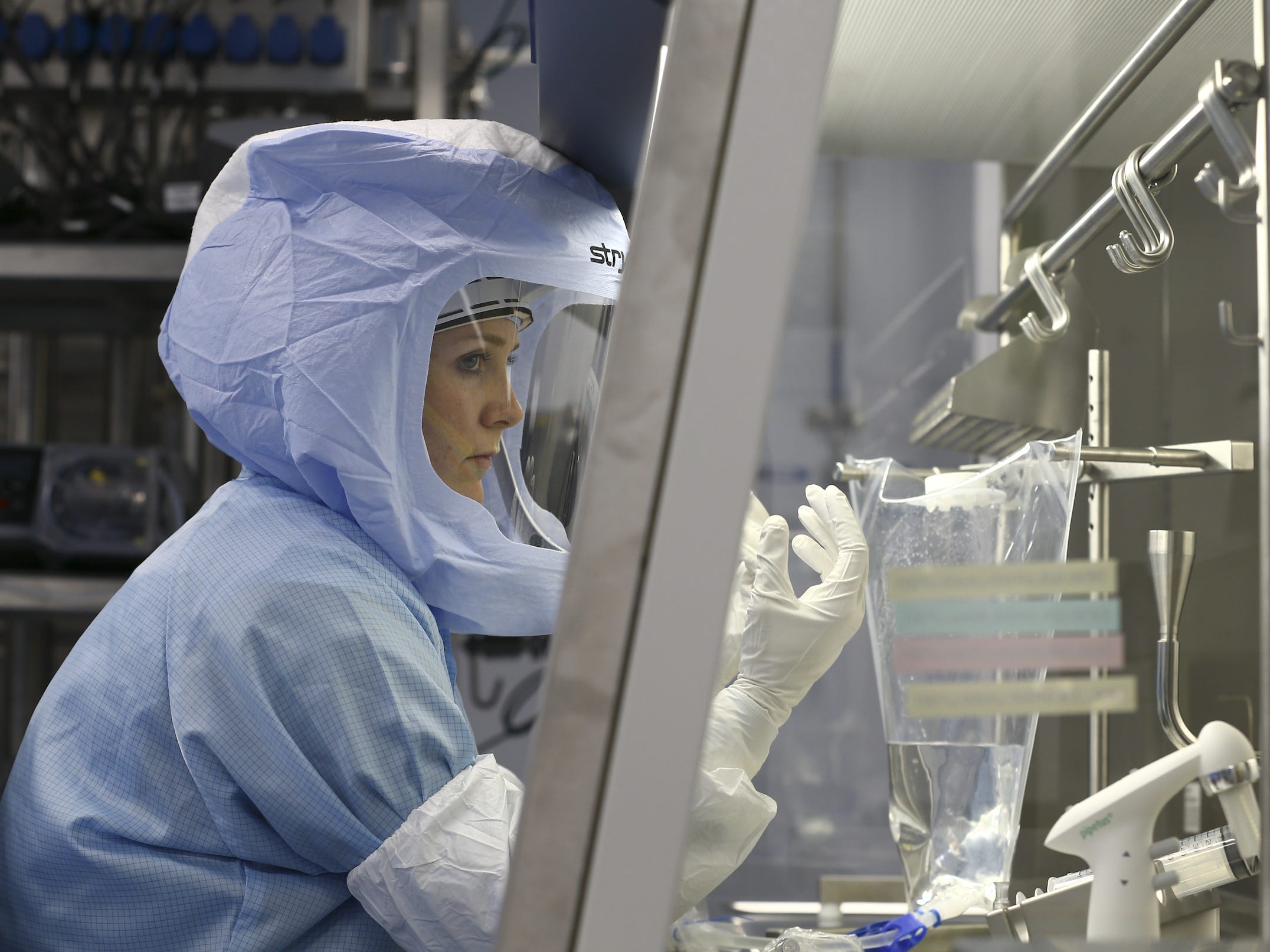 A person in a light-blue protective suit and helmet with face mask near laboratory equipment.