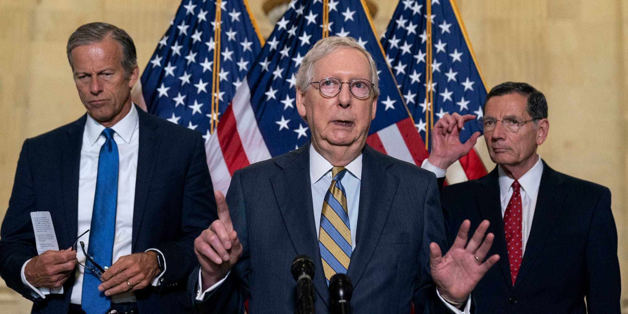 Senate Minority Leader Mitch McConnell stands between Senate Minority Whip Sen. John Thune, left, and Sen. John Barrasso with his hands raised, speaking with reporters on Capitol Hill.