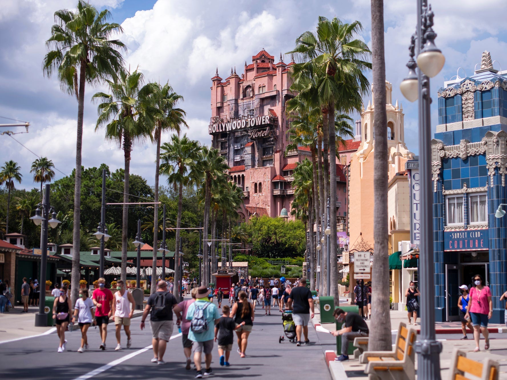 This image shows palm trees and colorful buildings among walking crowds at Disney World.