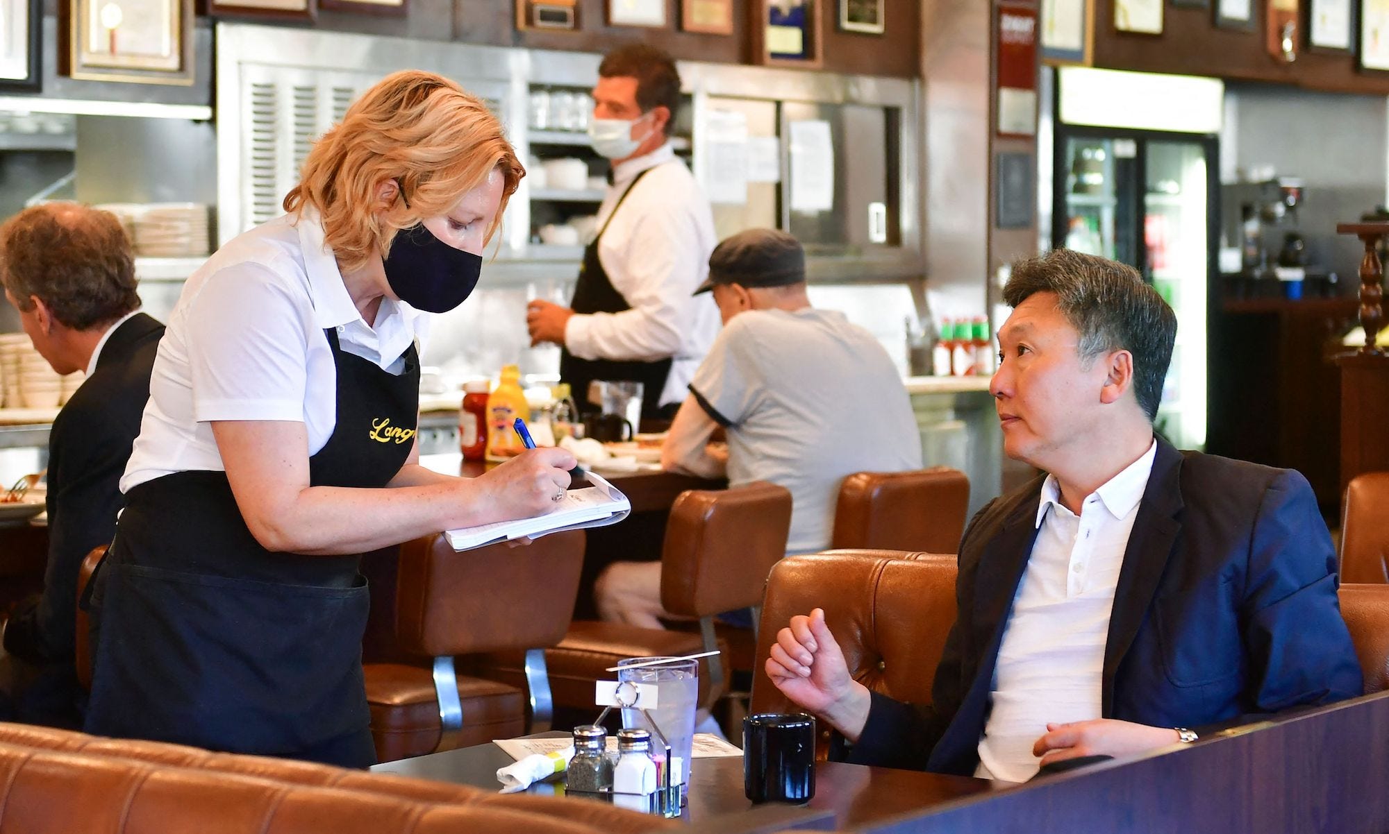 A waitress is taking a customer’s order at a table. There are other customers and another server in the background.