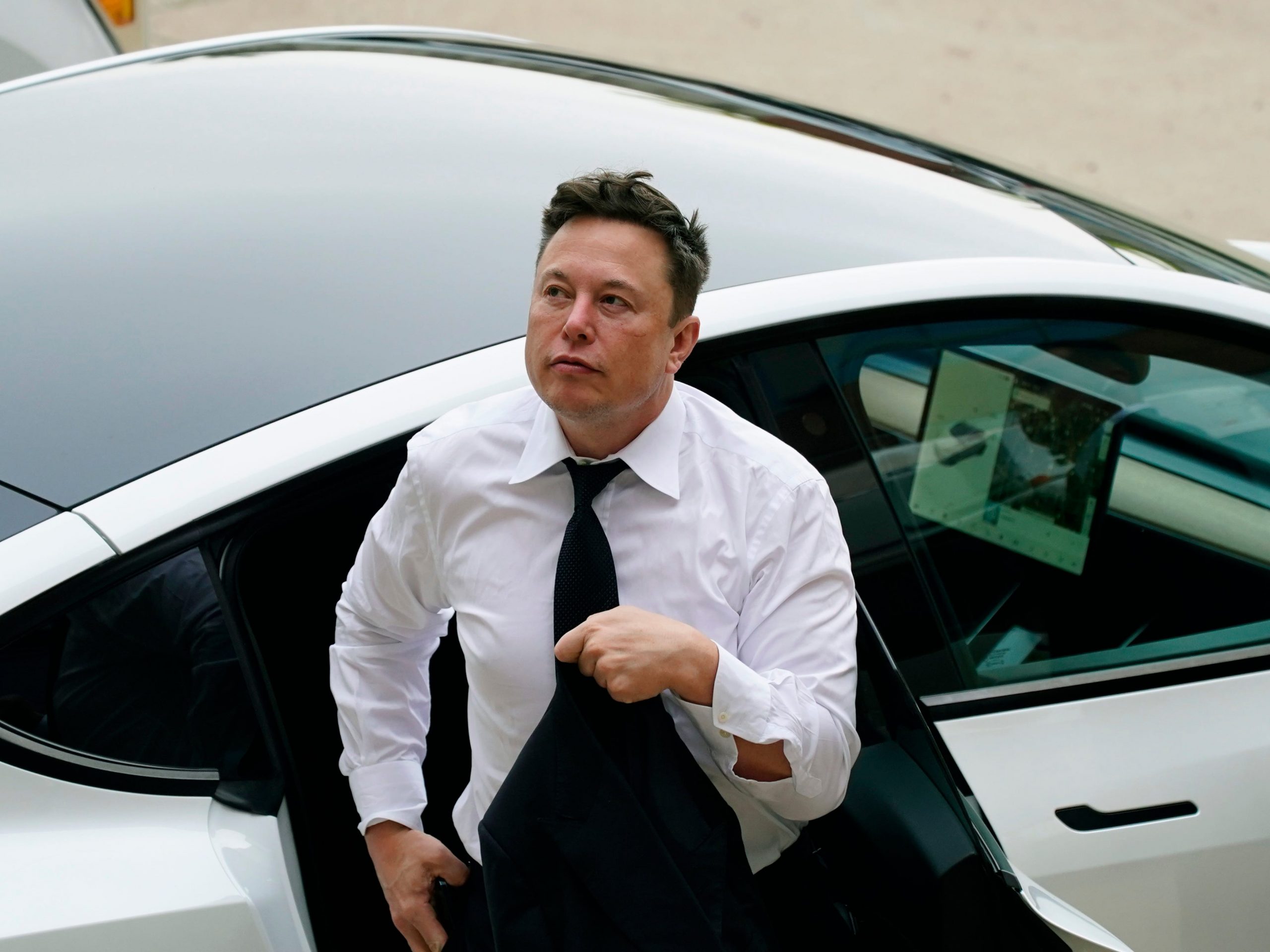 Tesla CEO Elon Musk in a white shirt and tie exits the backseat of a white Tesla