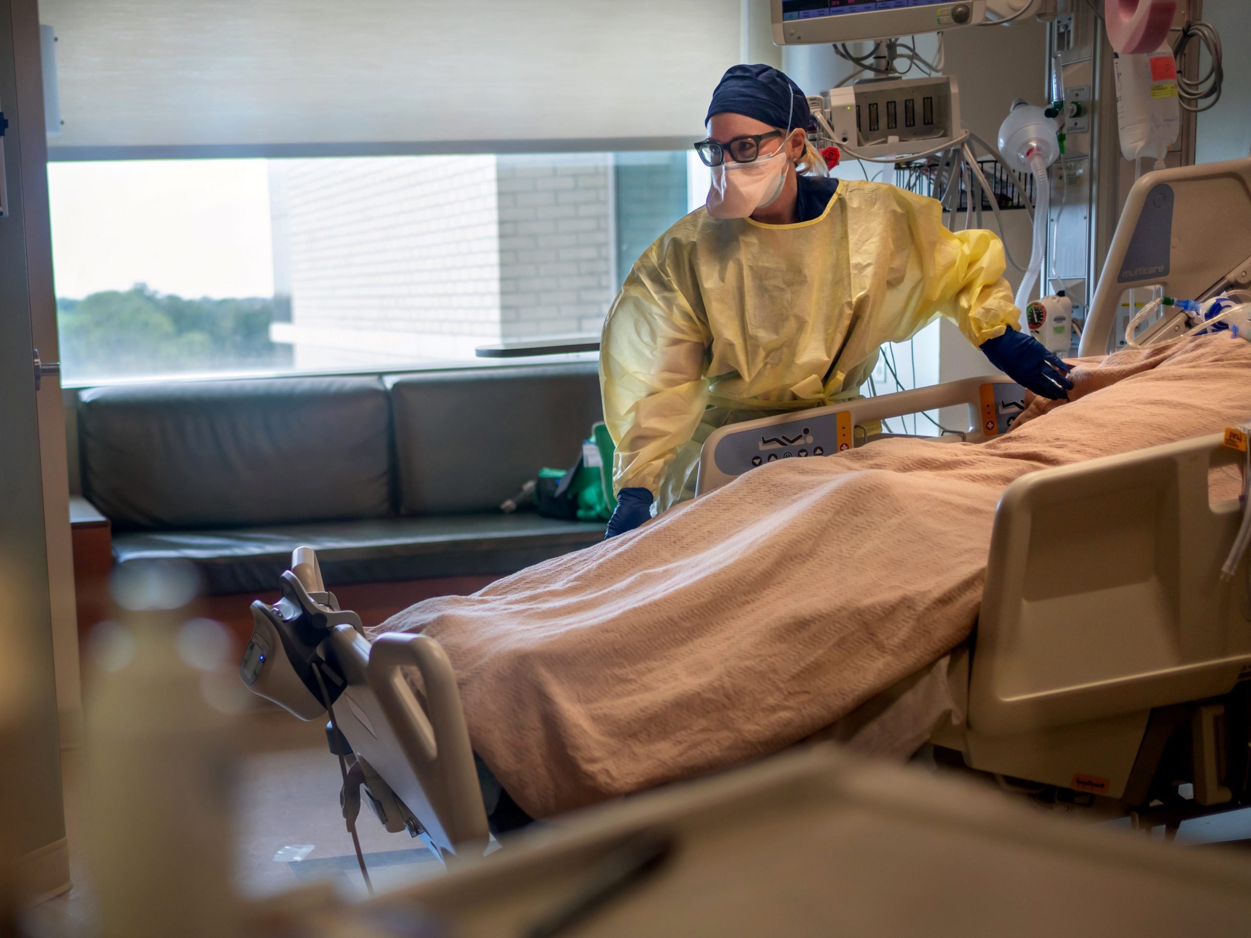 A doctor wearing full protective equipment treats a patient in an ICU bed.
