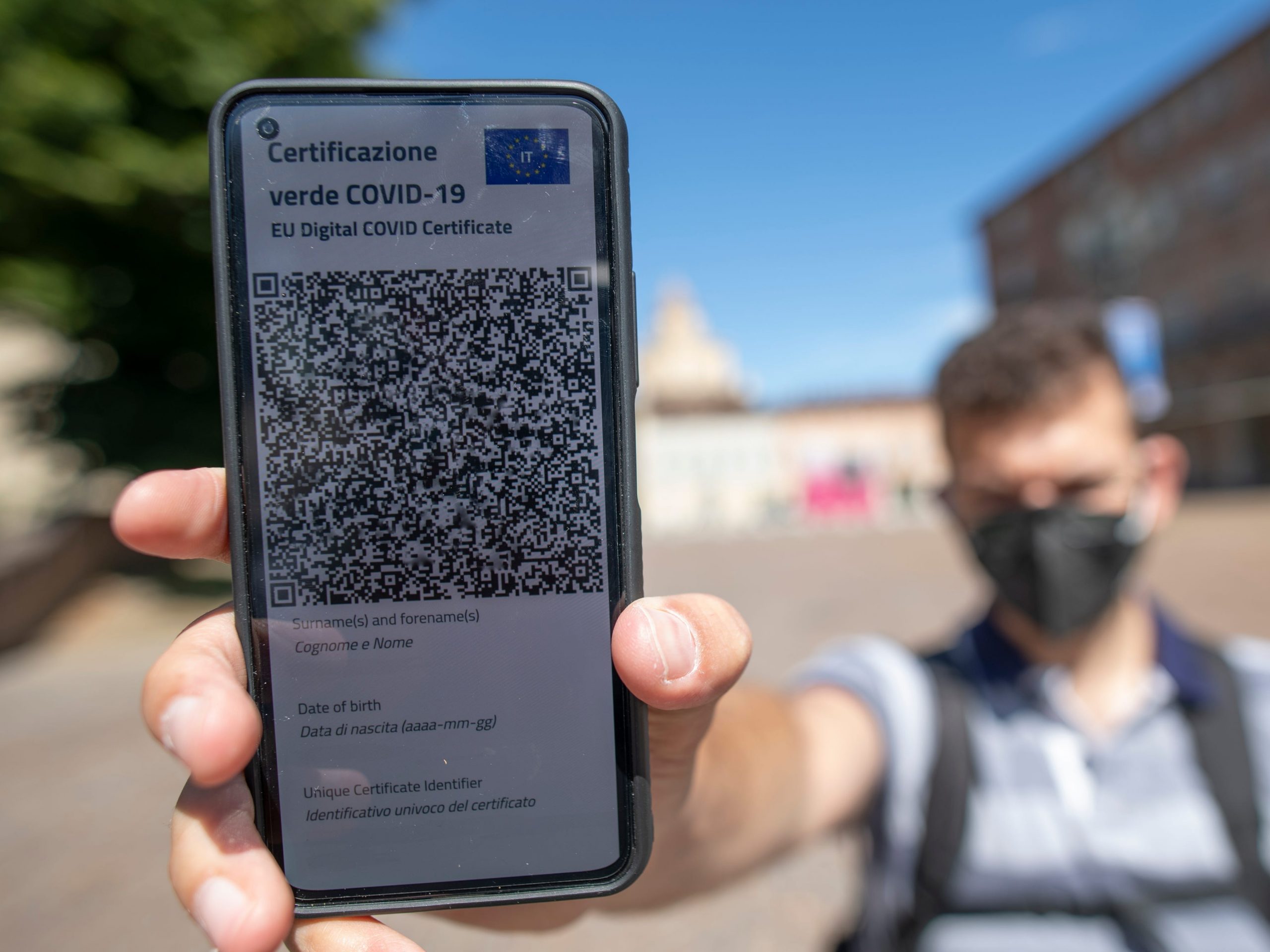 Masked man holding phone displaying QR code for Italian vaccine passport