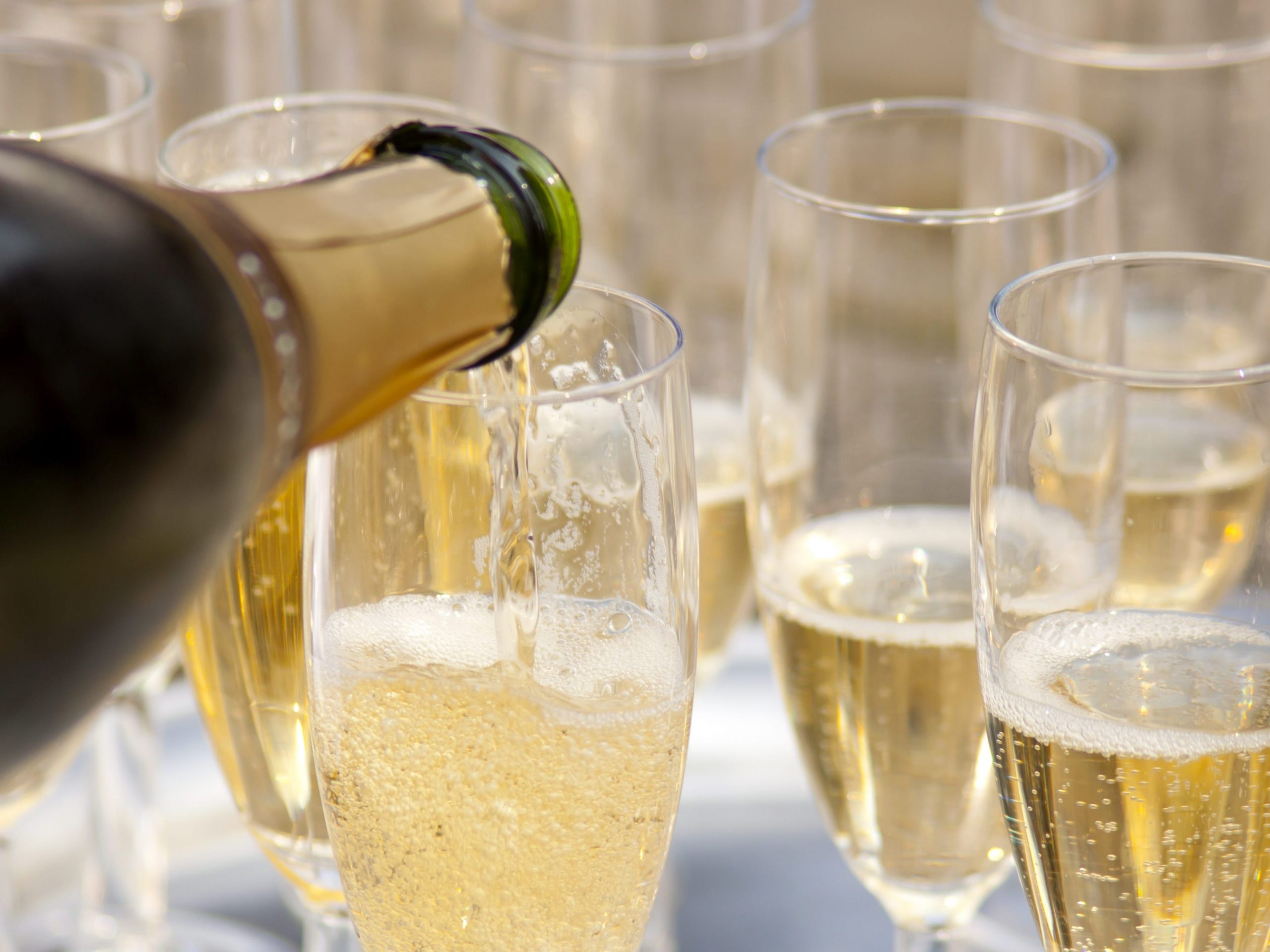 Champagne being poured into a glass on a table of filled flutes