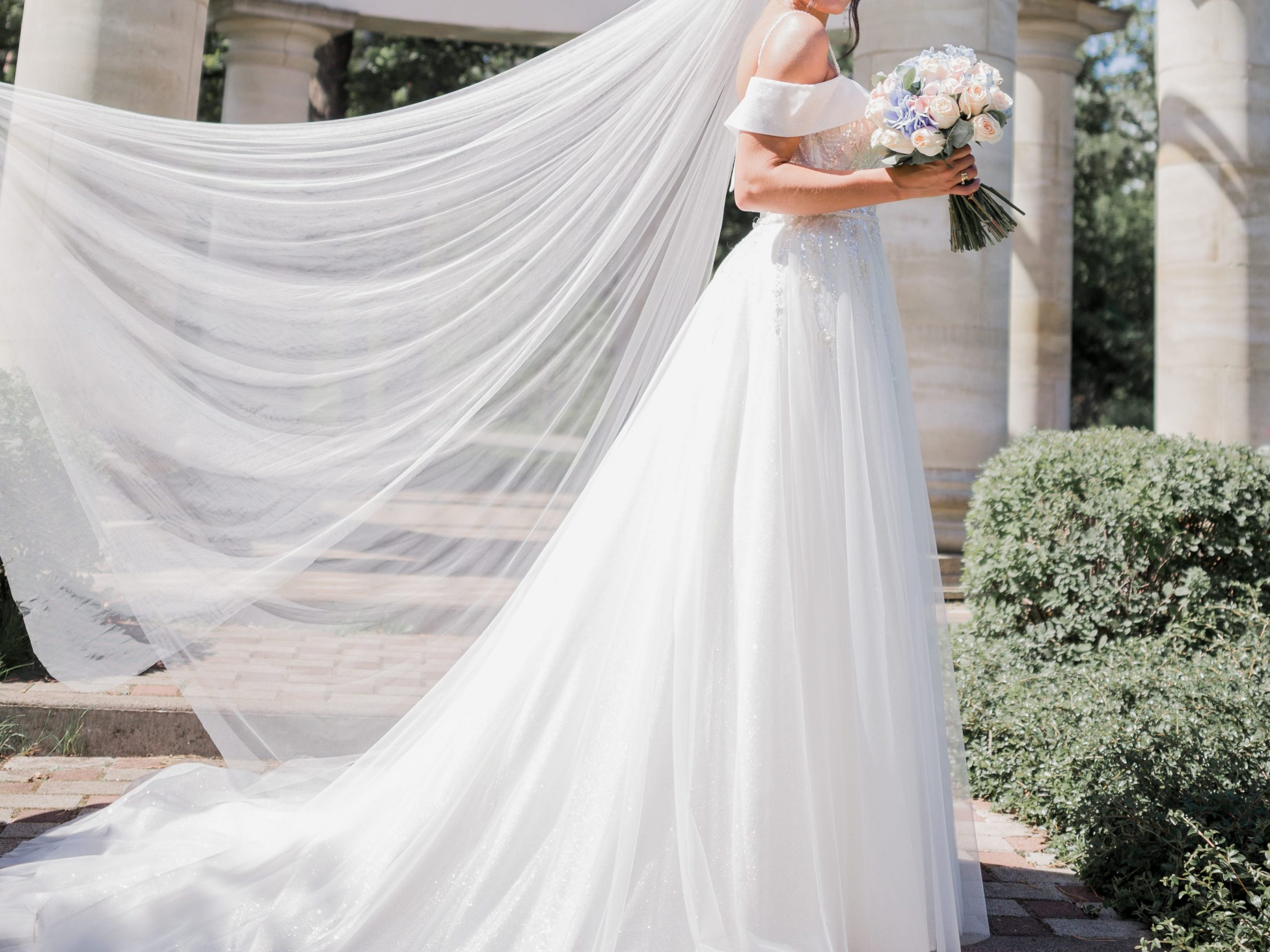 A bride wearing a long veil and holding a bouquet